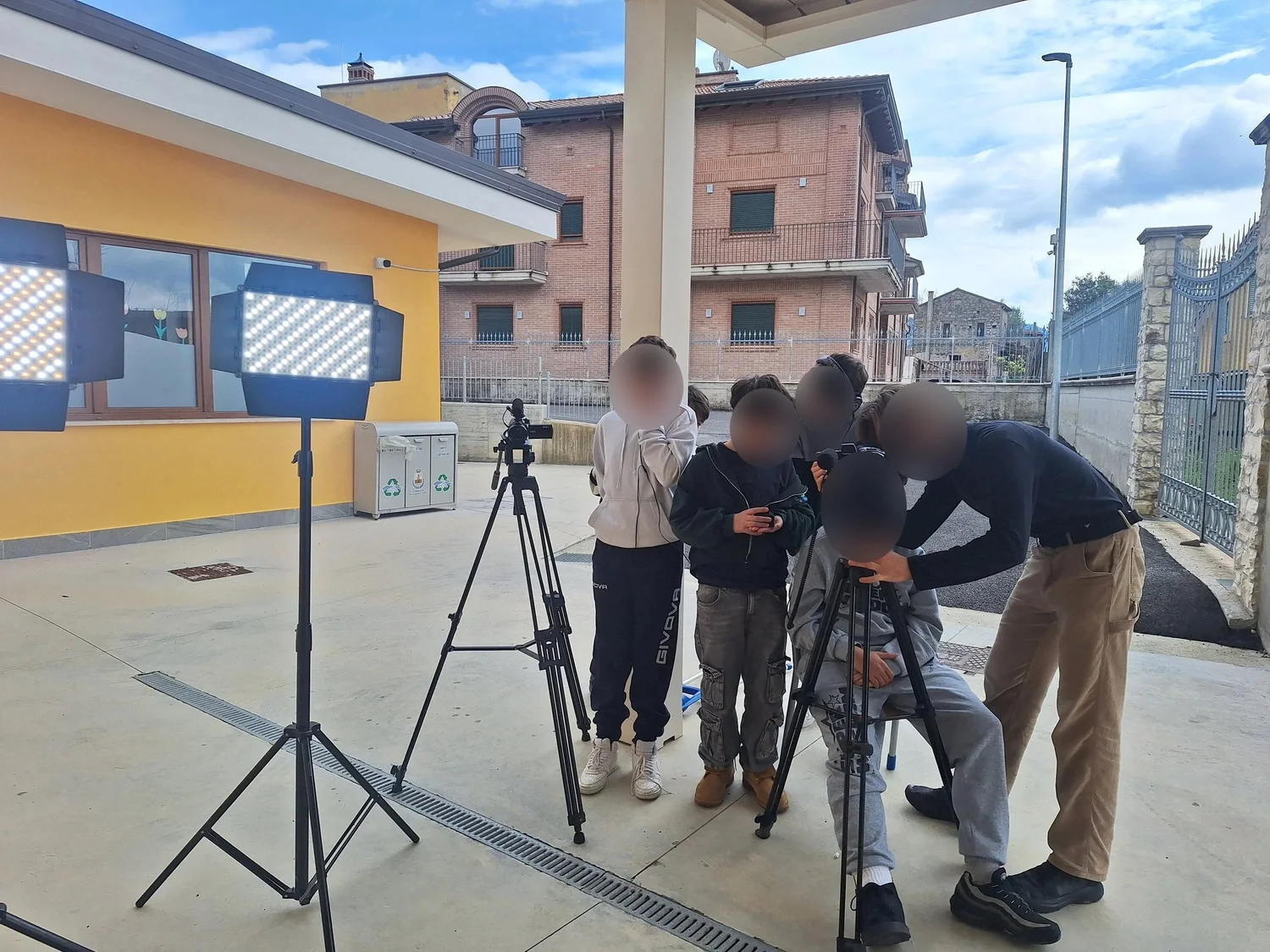Ripresa all'aperto davanti alla scuola: i ragazzi alla macchina da presa, con i pannelli luce