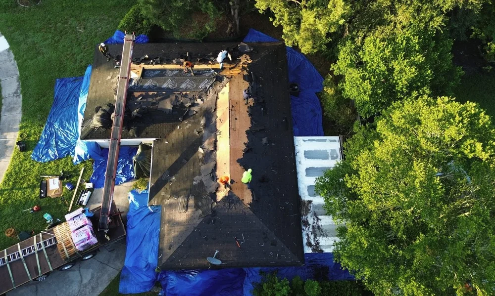 Aerial view of a 7V roof tear-off underway with the yard protected by blue tarps