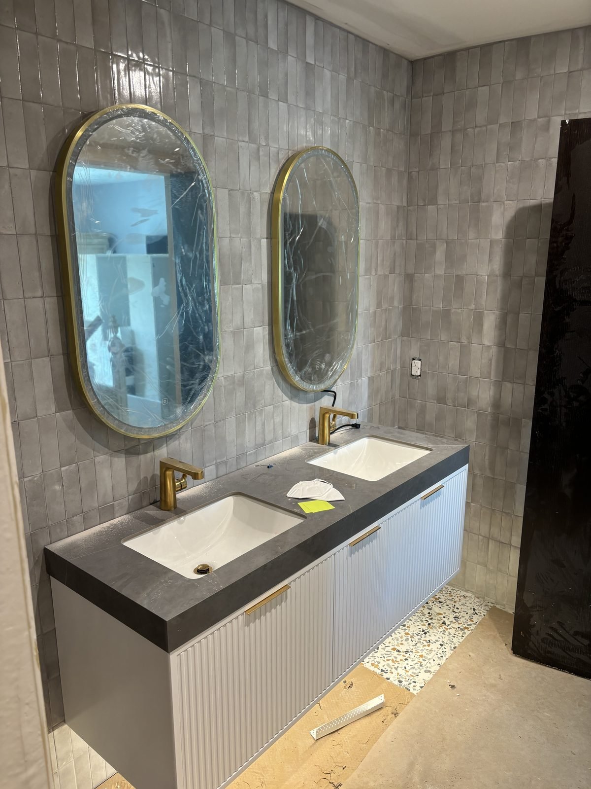 Renovated bathroom with double vanity, grey tile and gold fixtures