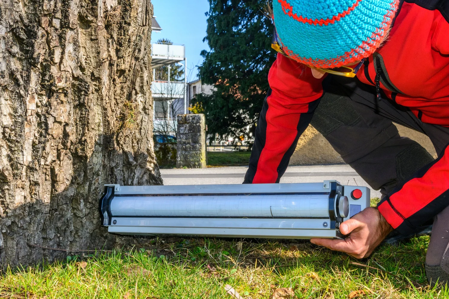 Illustrative stock photograph showing inspection equipment positioned at the base of a tree by a person in a red jacket.
