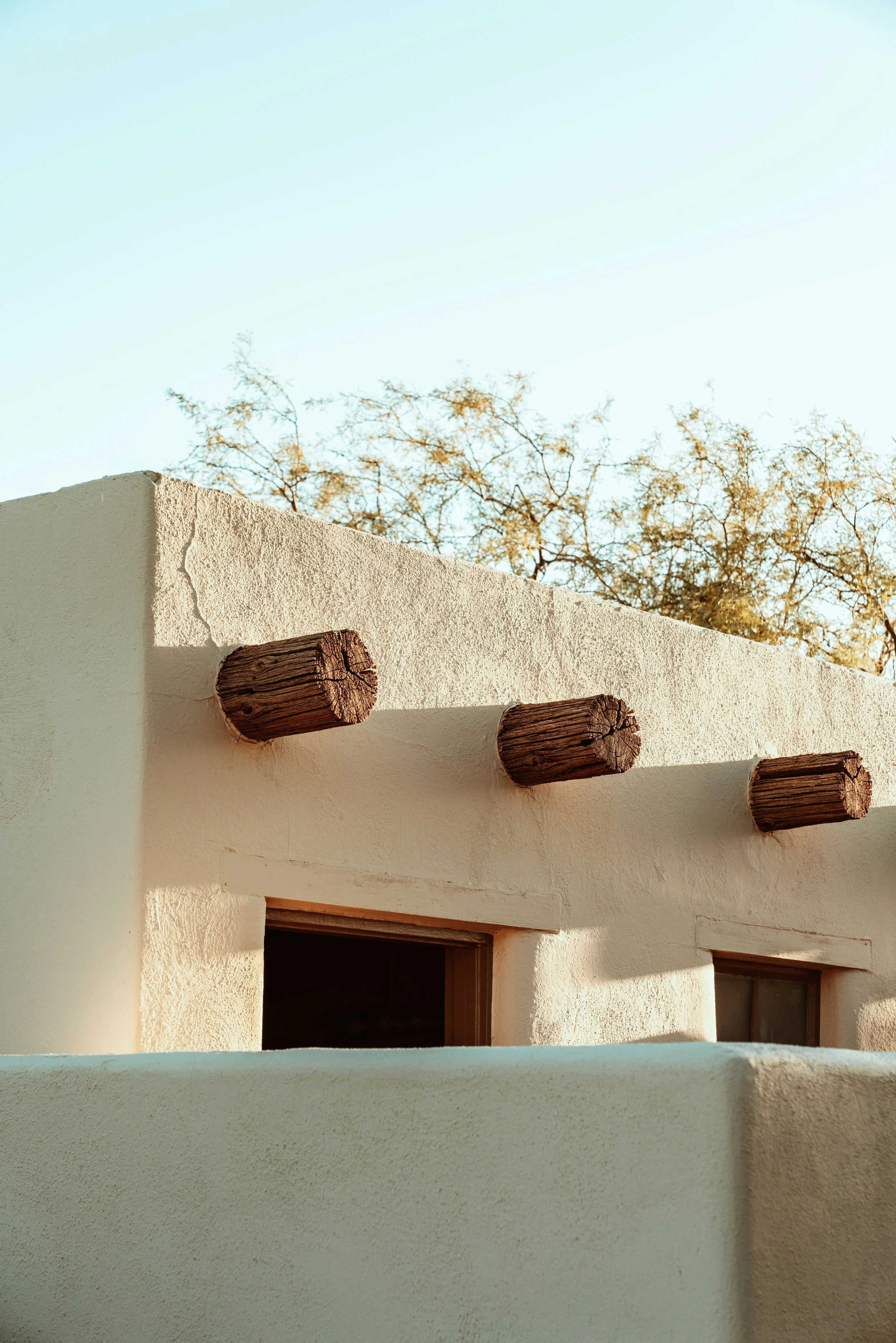 Adobe-style stucco building with exposed wood beams against a clear sky