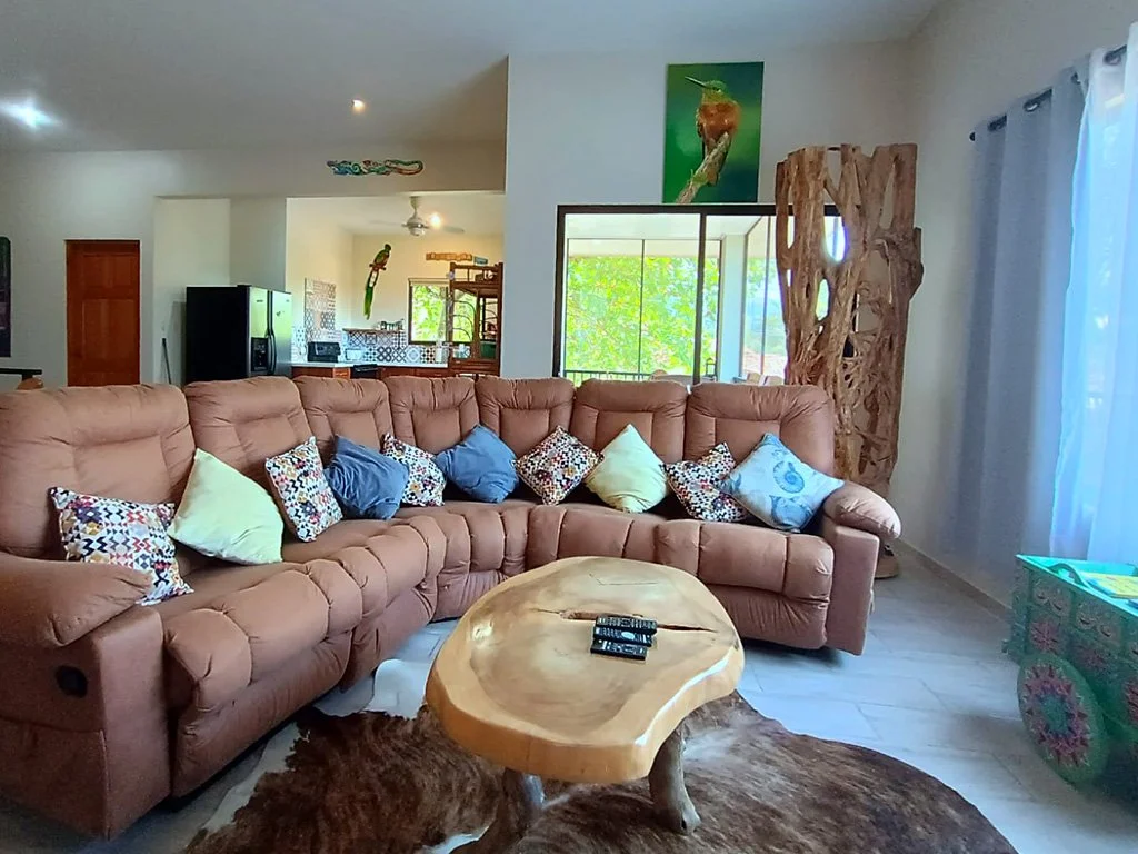 Spacious living room at Hermosa Duplex in Playa Hermosa featuring a sectional sofa, natural wood table, and open-concept design with tropical garden views.