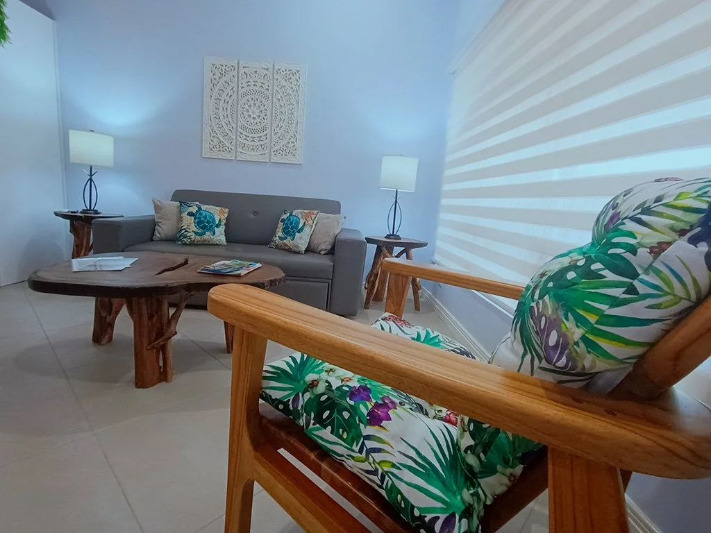 Modern tropical-style living room with wooden armchair and cozy sofa at Beach apartment COCO 49 in Jacó, Costa Rica.