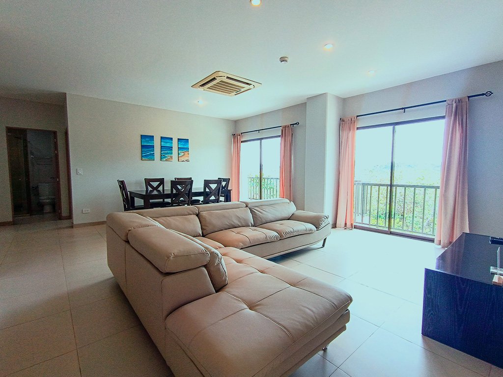 Bright open living and dining space with large sofa and balcony view at Jacó Bay vacation rental in Jacó, Costa Rica.
