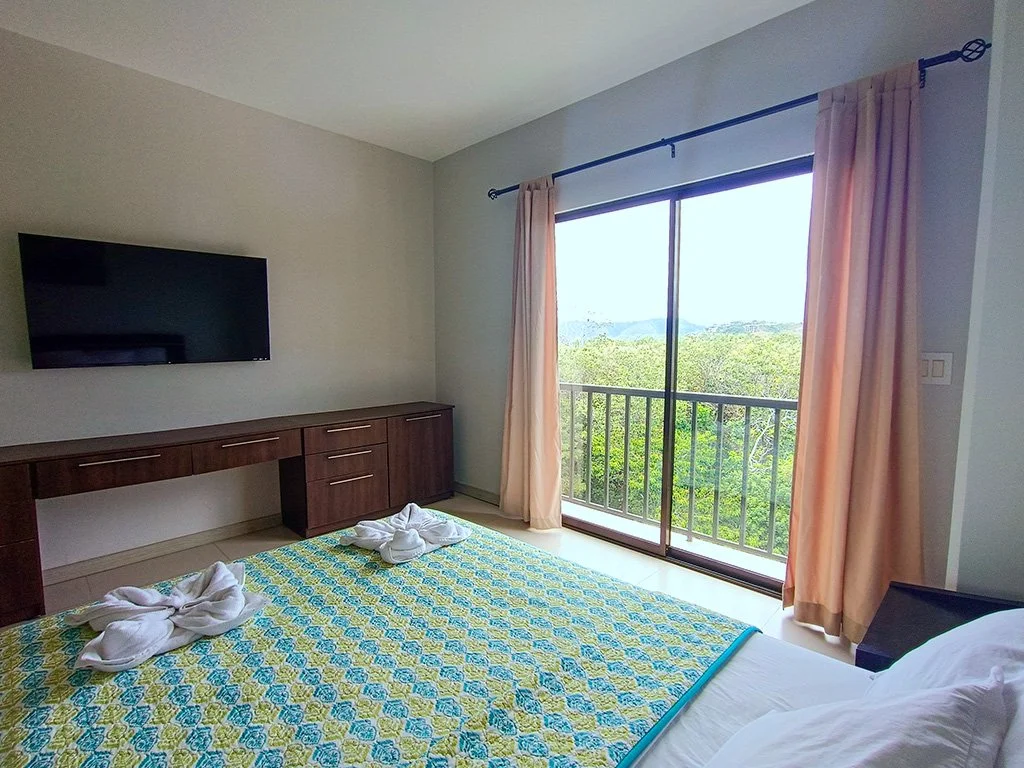 Bright bedroom with private balcony overlooking lush tropical landscape at Jacó Bay vacation rental in Jacó, Costa Rica.