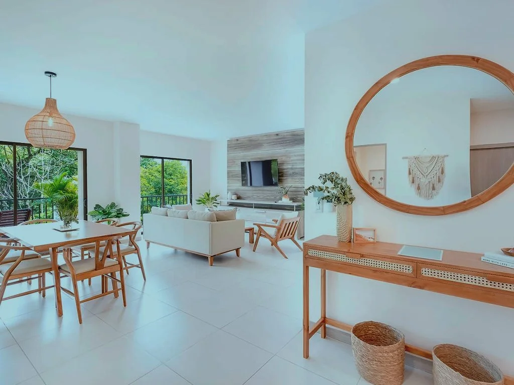 Modern open concept living and dining area at Jacó Bay condominium with natural wood furniture and large windows facing tropical views.