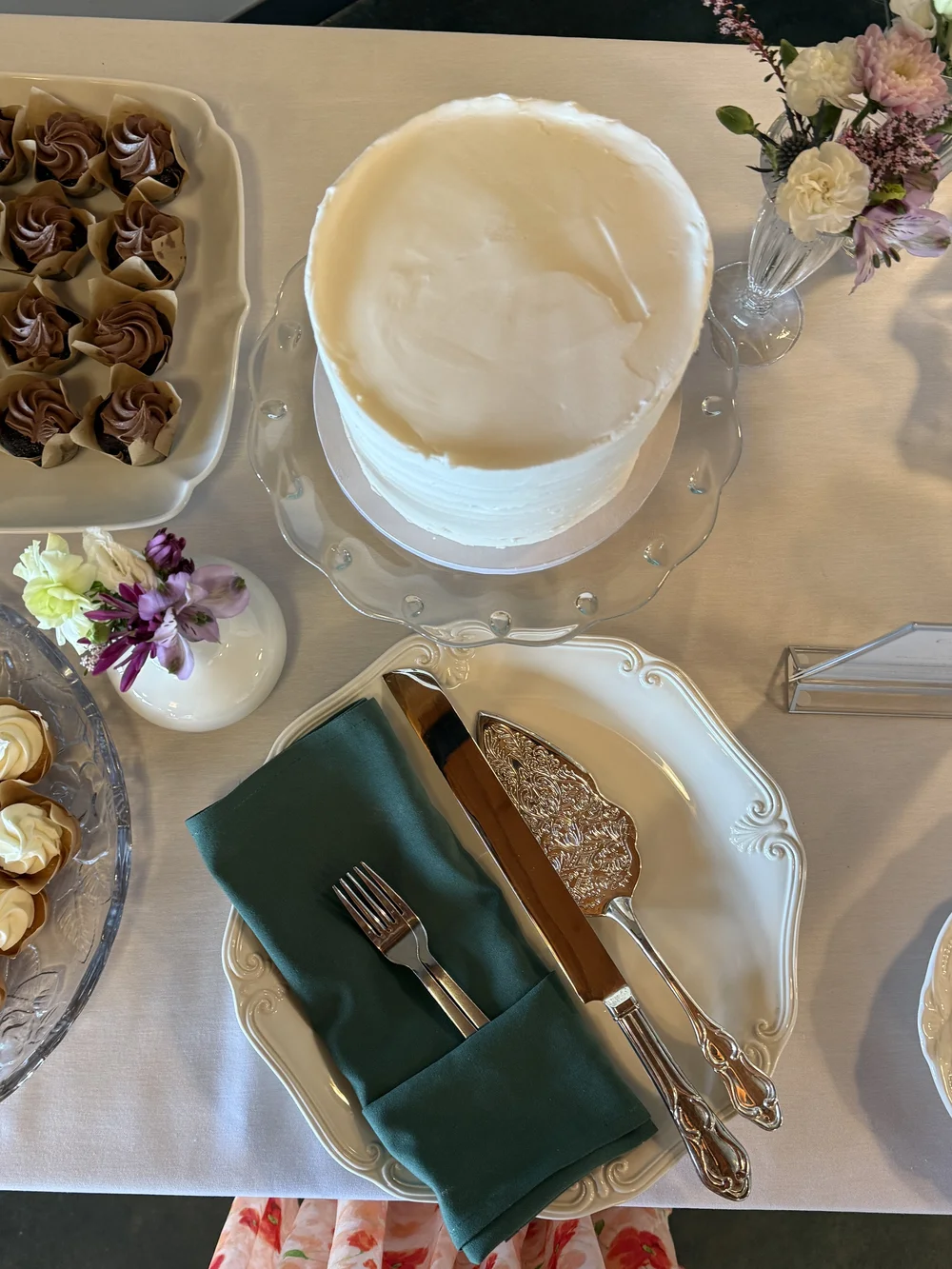 A dessert table with a white cake, petit fours and a green linen napkin