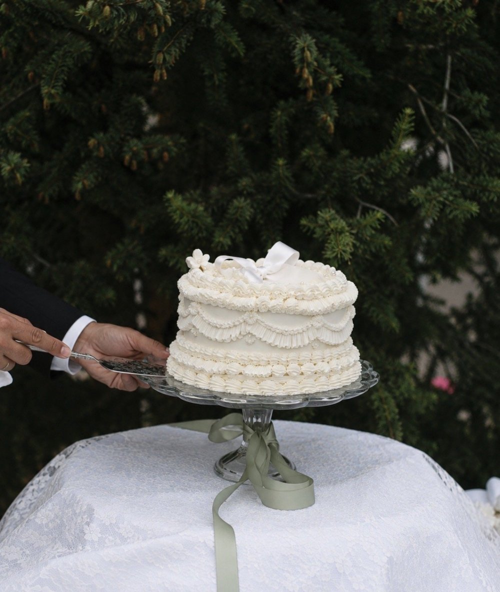A ruffled wedding cake on a glass stand tied with green ribbon