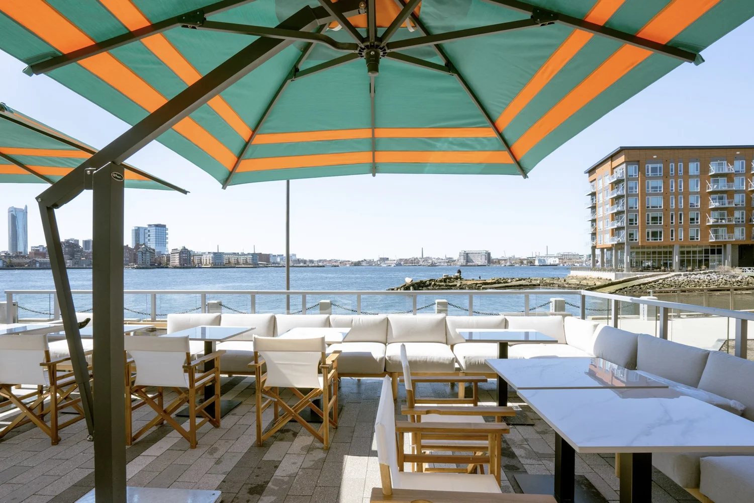 Lounge seating under striped umbrellas on the waterfront patio at La Tavernetta by MIDA