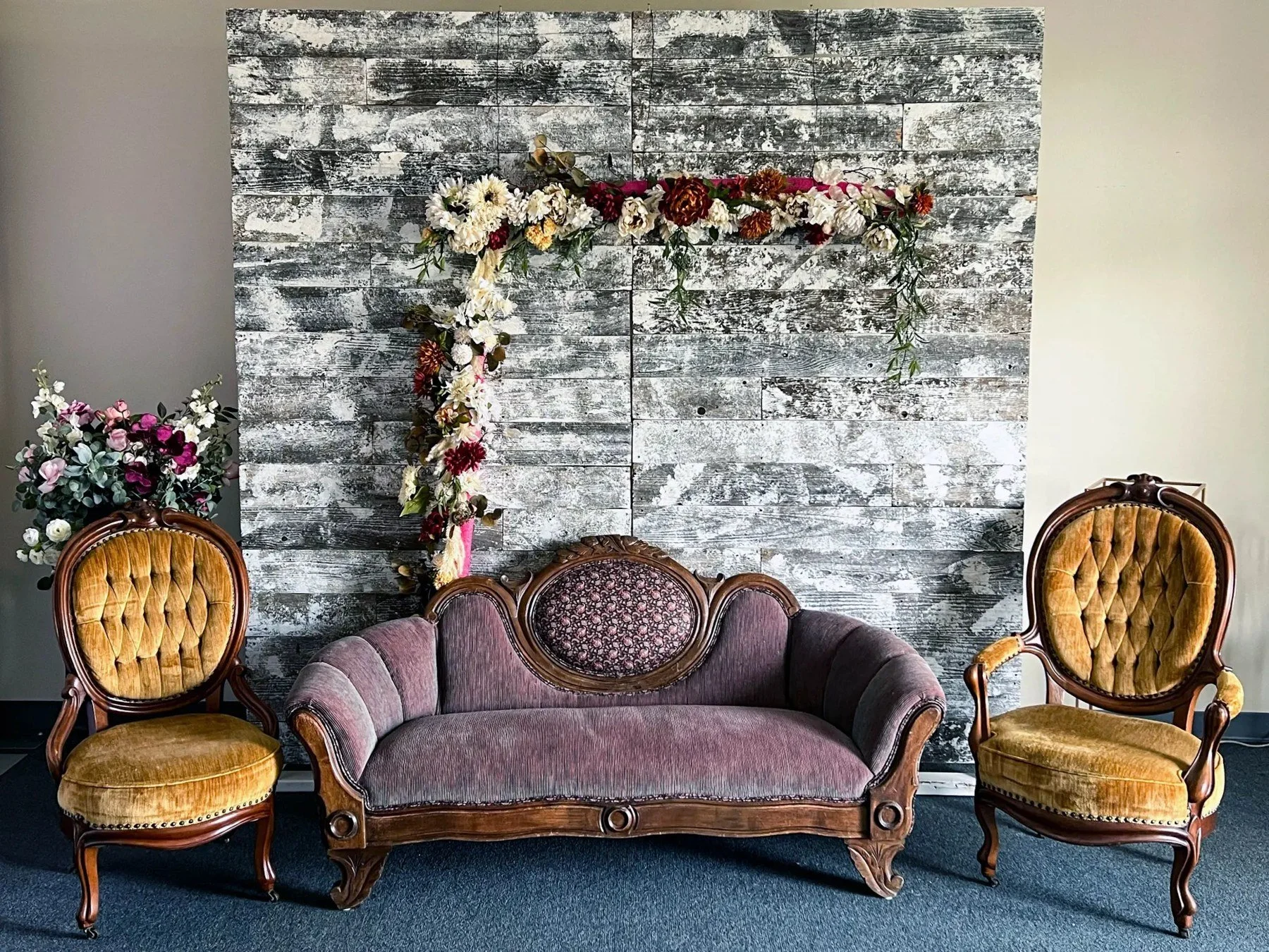 White barn wood backdrop with a maroon couch and gold chairs.