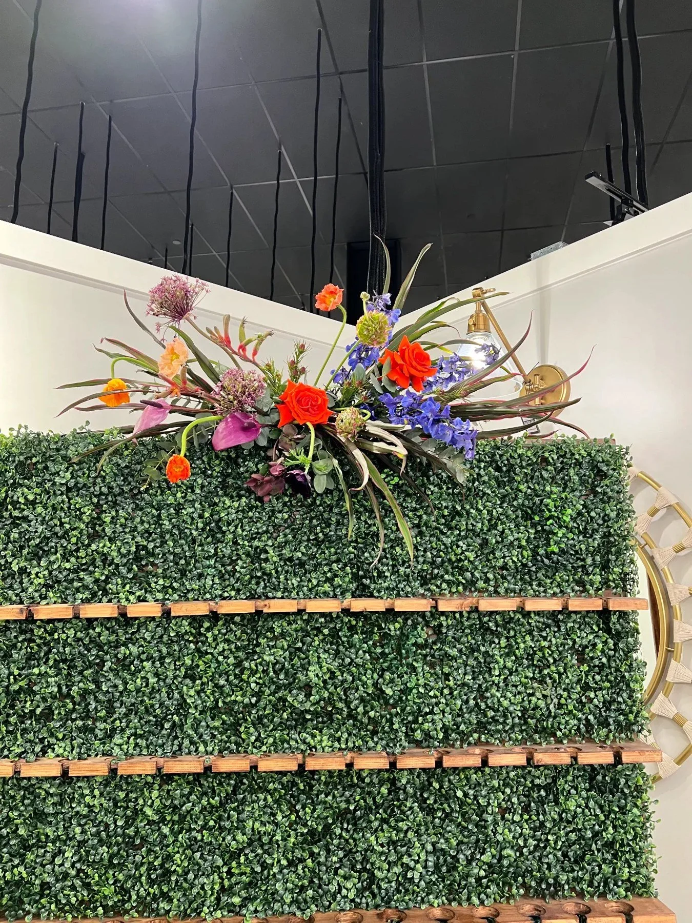 Bright orange, purple and blue floral arrangement across the top of a boxwood champagne wall.