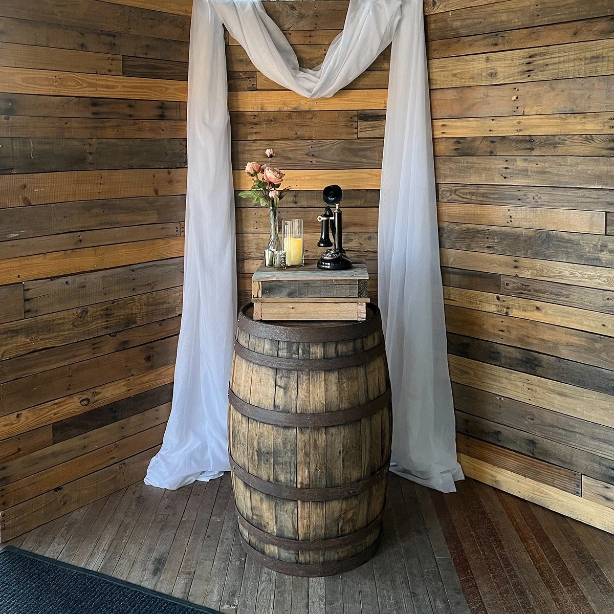Pallet Wall styled with white draping, a whiskey barrel and a vintage telephone.