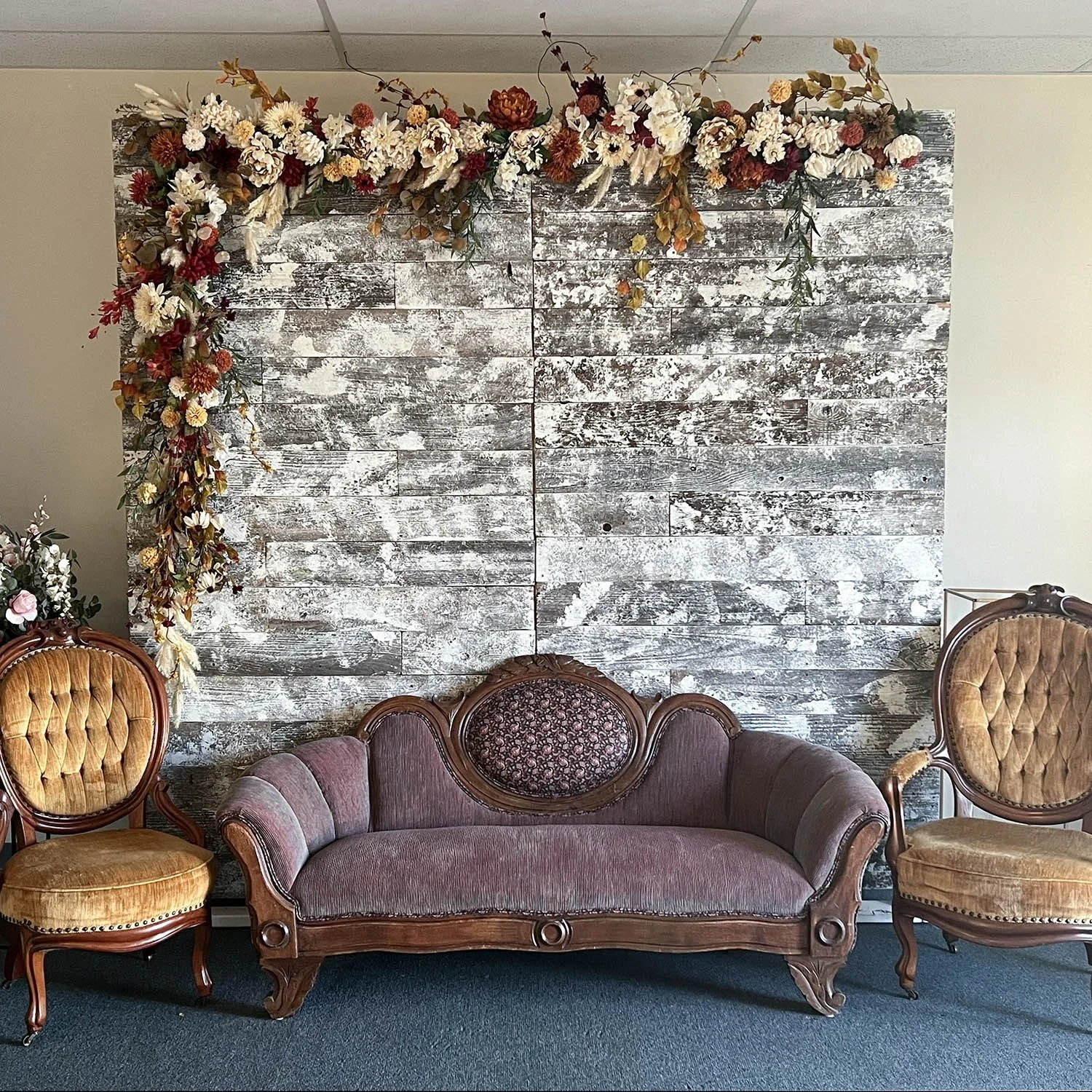 Floral swag draped across the top and down the left side of a whitewashed wood wall, above an antique loveseat and two chairs.