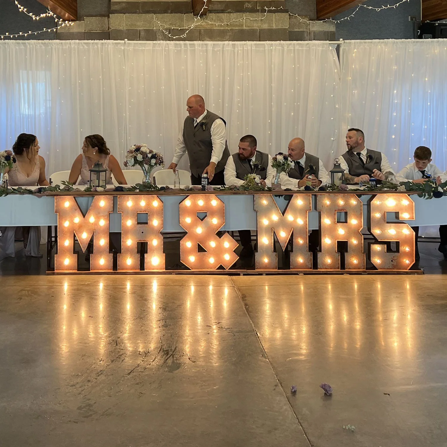 Double drape with lights behind a head table and a lighted Mr and Mrs sign in front.