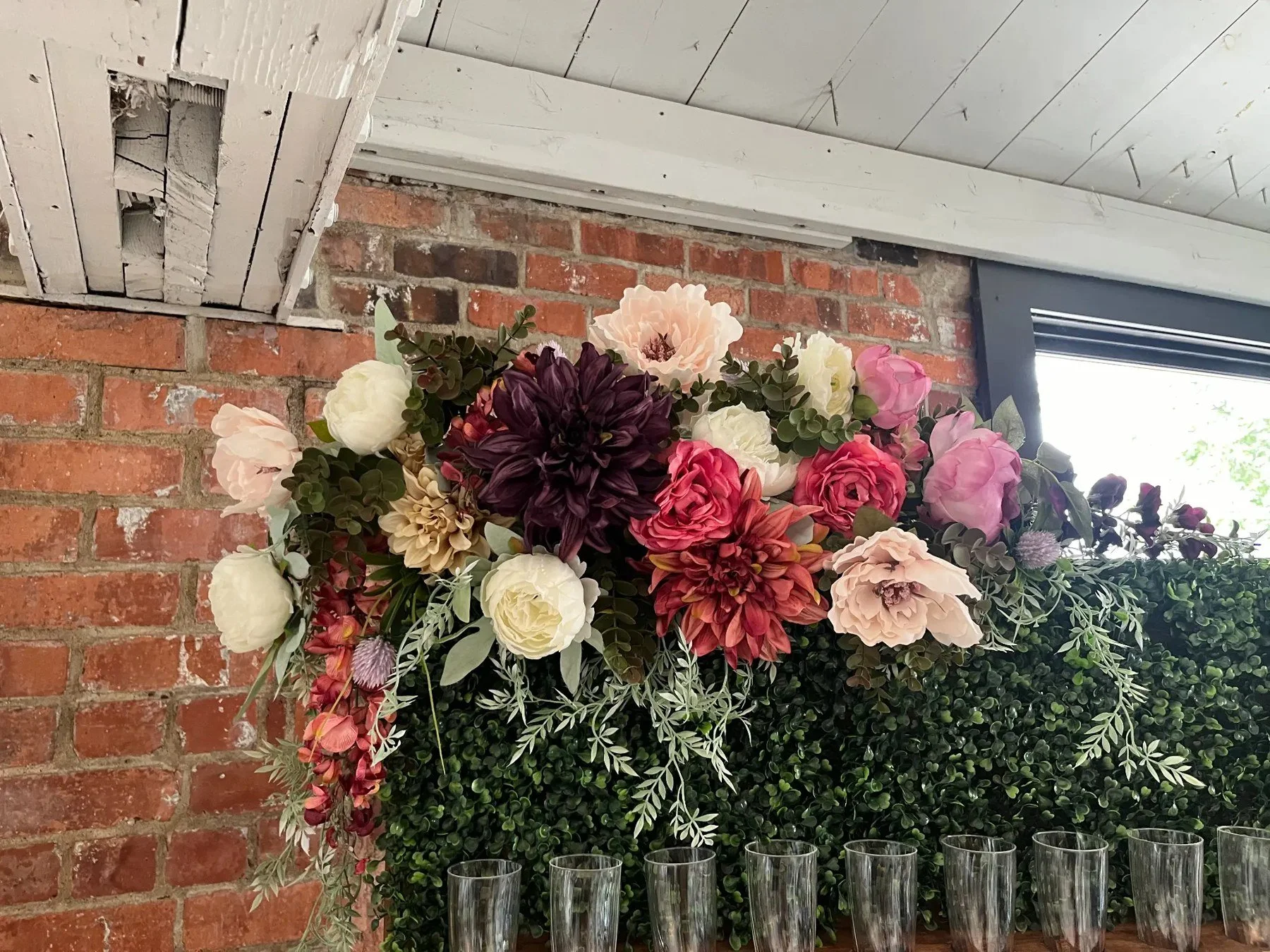 Pink, burgundy, ivory and blush silk florals with trailing greenery across a boxwood champagne wall.