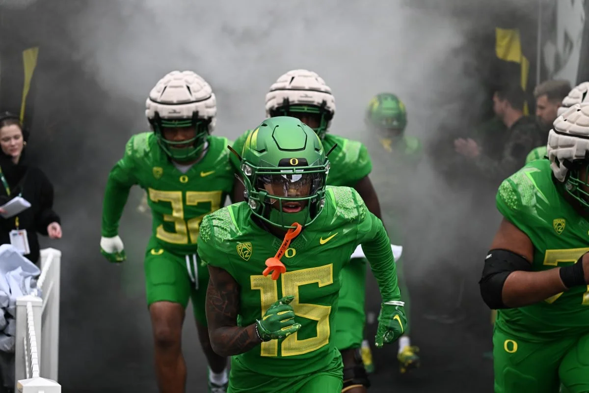 Oregon football players in green uniforms emerge through smoke onto the field.
