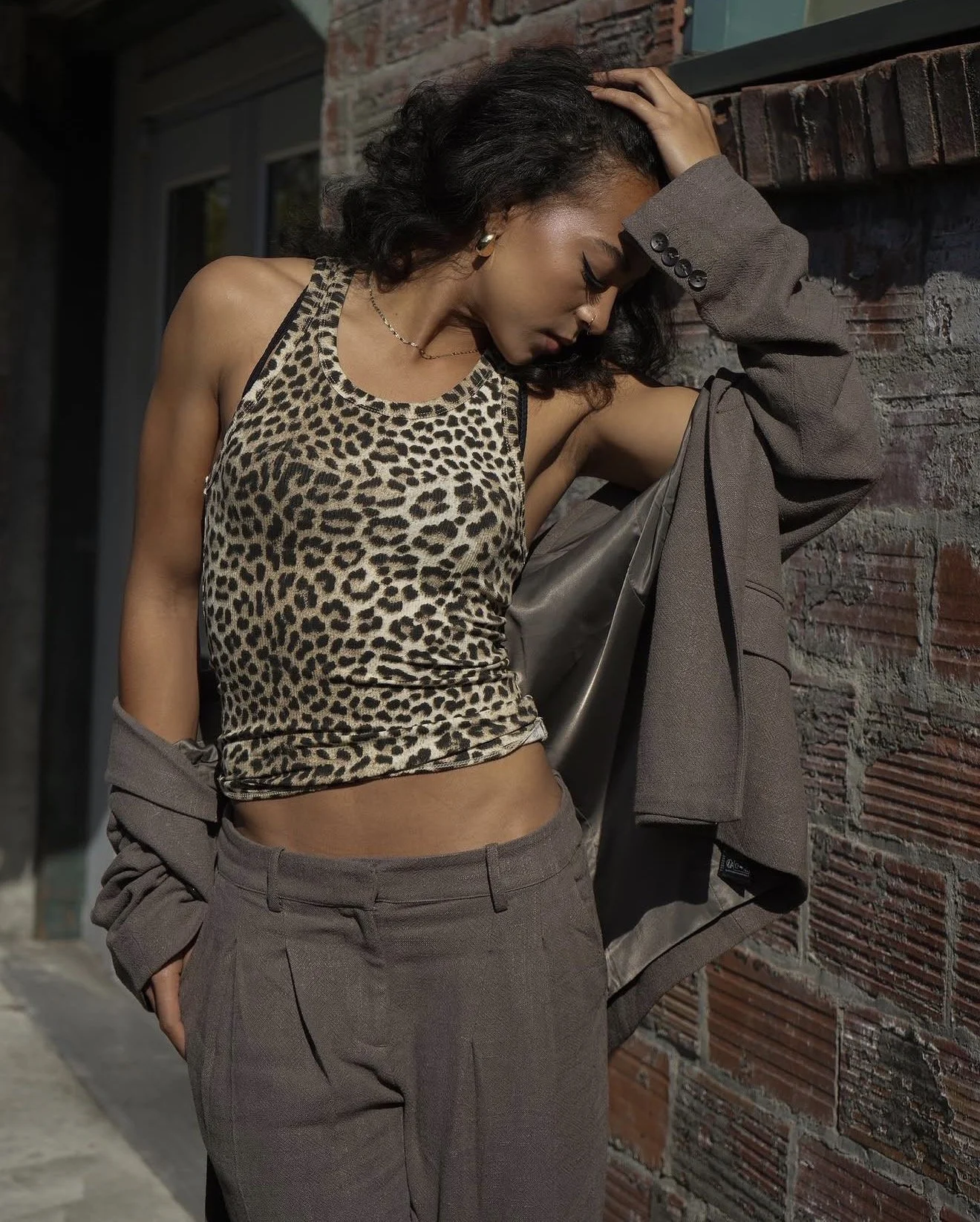 Fashion portrait of a woman lifting her hair beside a brick wall.