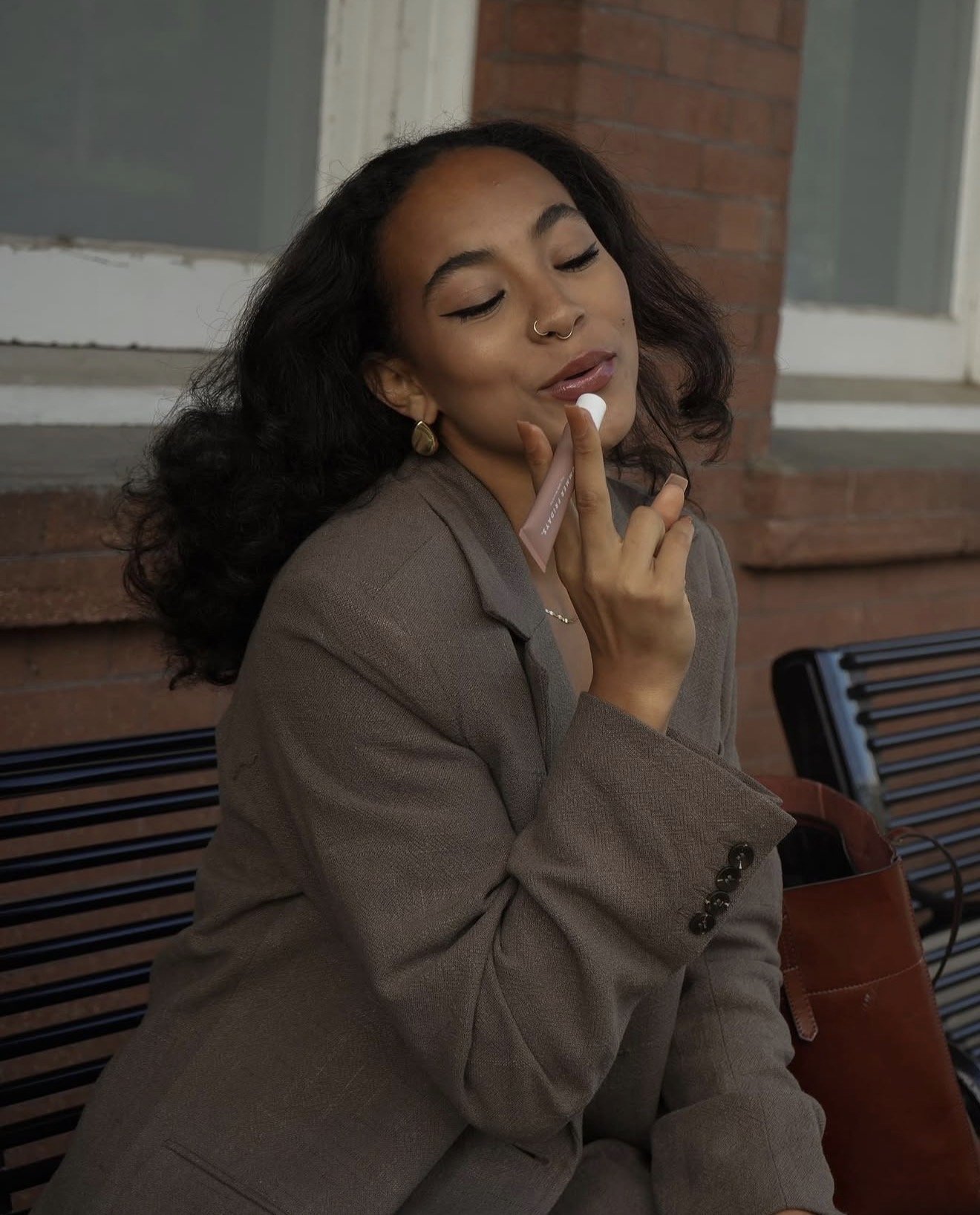 Close-up fashion portrait of a woman in a gray blazer with her hand near her face.