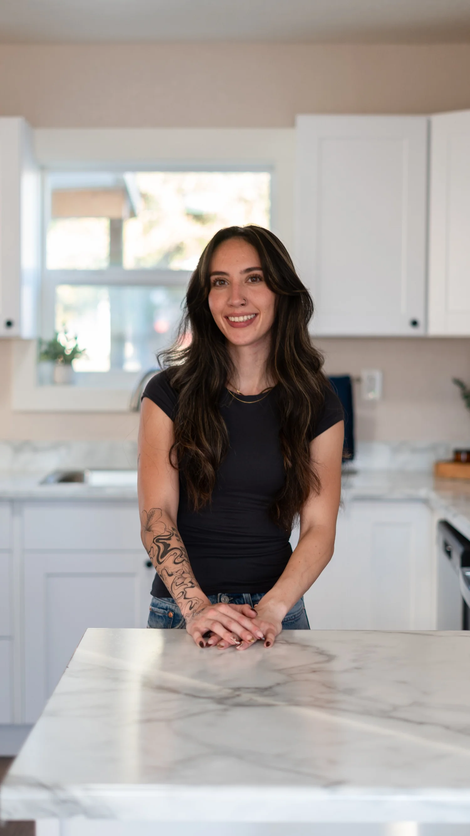 Portrait of a smiling woman with her hands resting on a kitchen island.