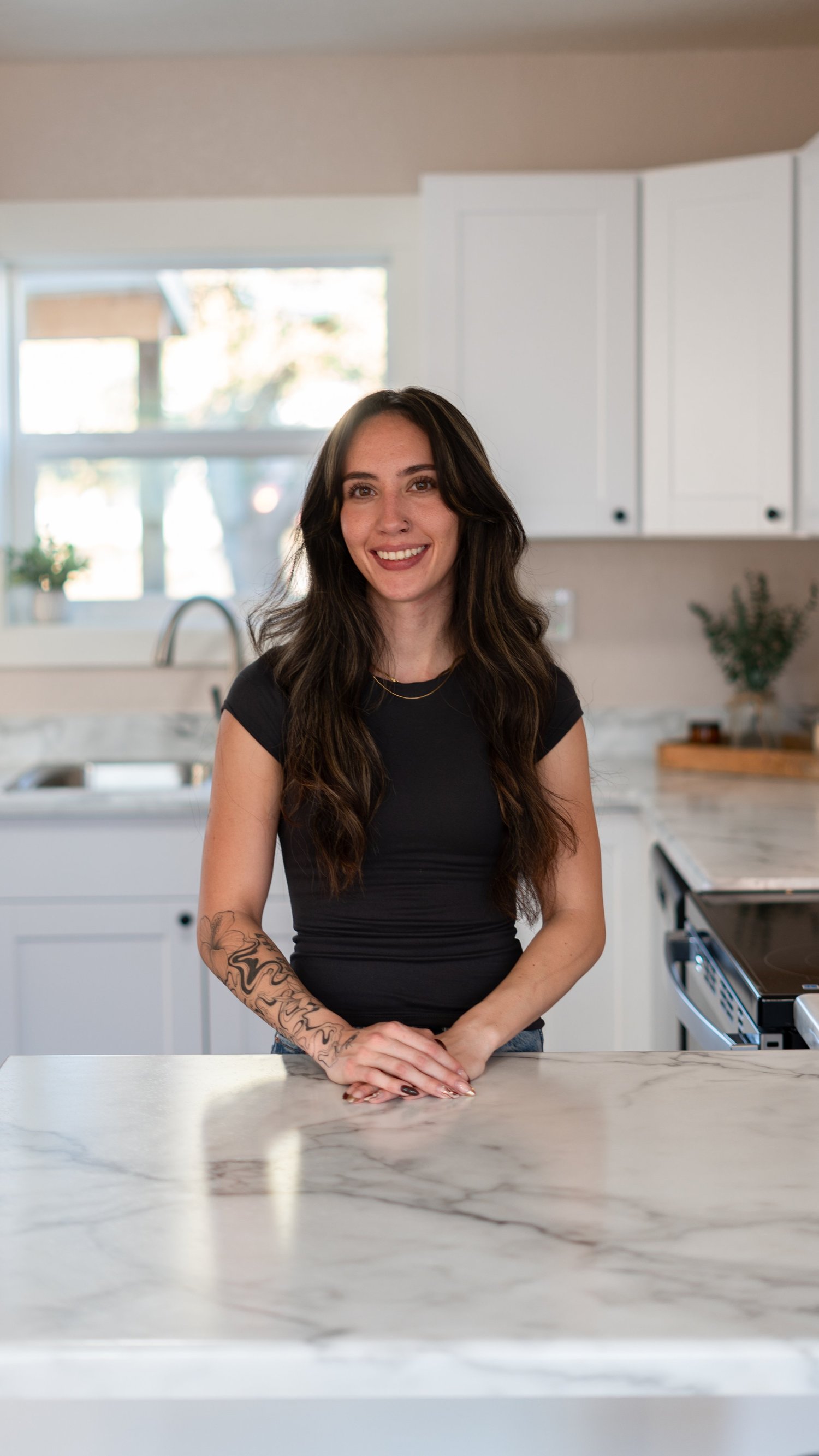 Portrait of a woman in a black top standing behind a marble kitchen island.