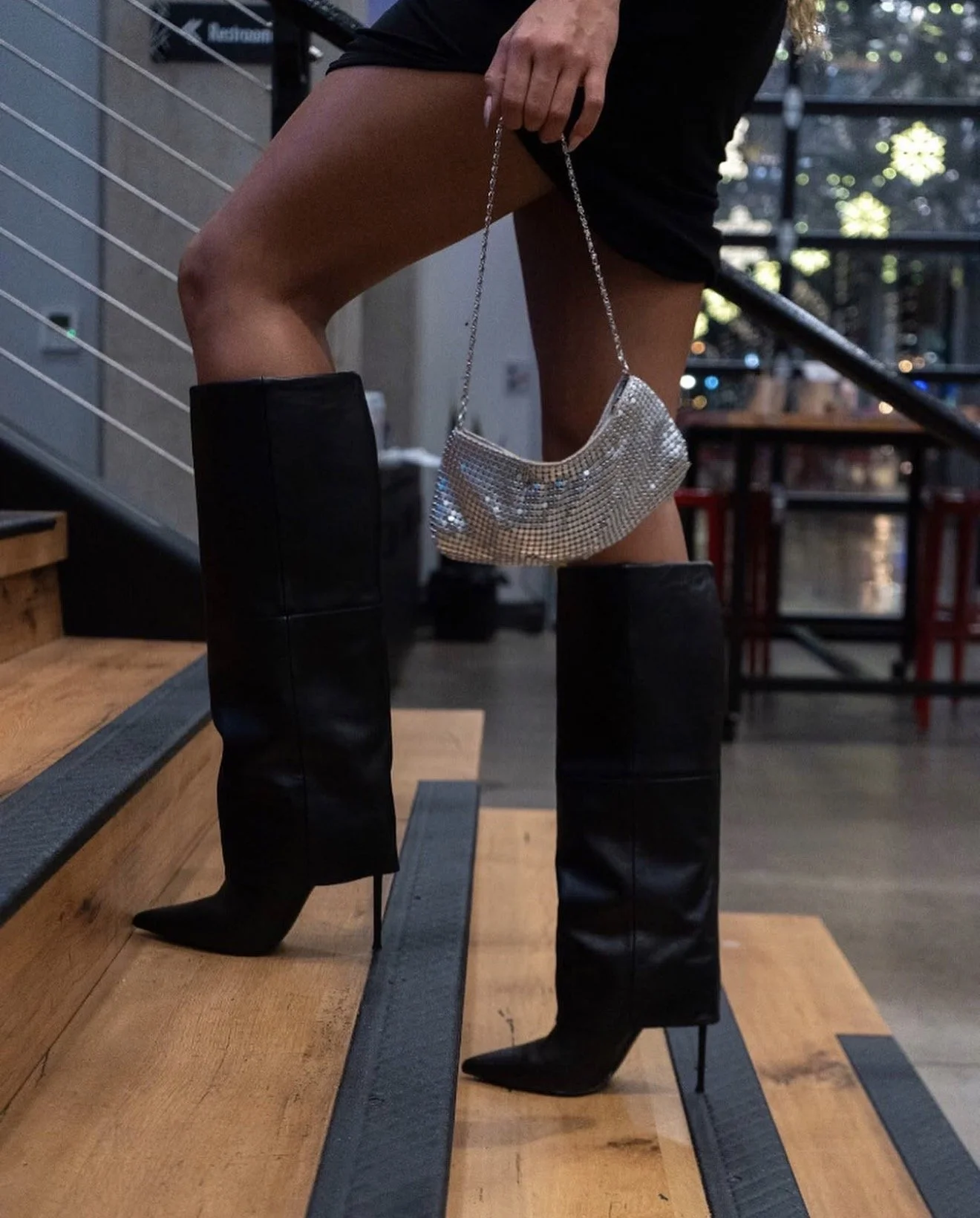 Detail of tall black boots and a white handbag on indoor steps.