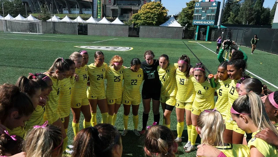 Oregon soccer team gathers in a circle on the field.