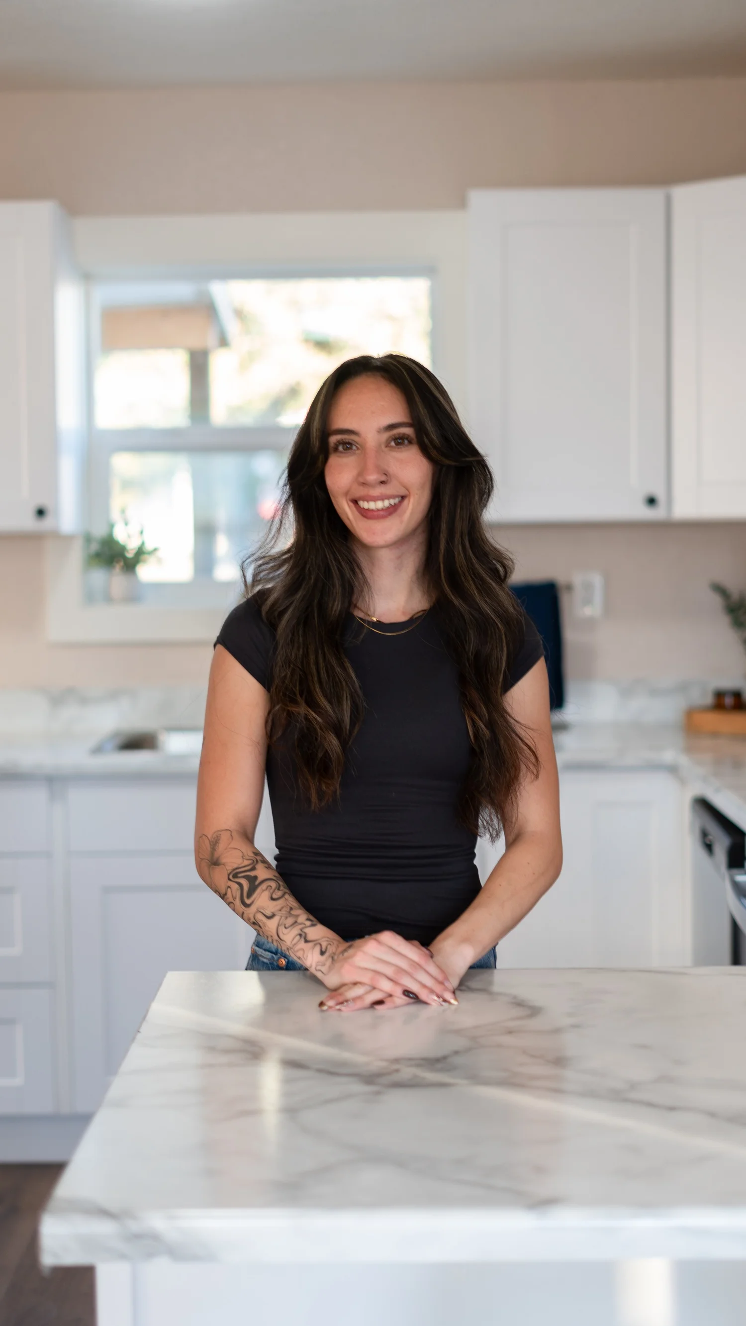 Front-facing portrait of a woman smiling behind a kitchen island.
