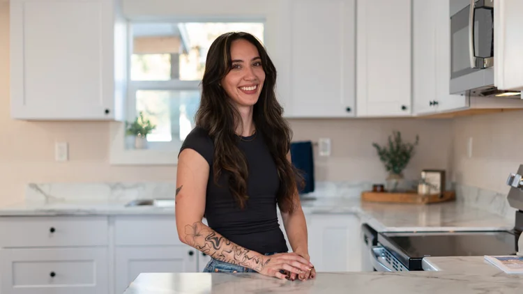 Professional portrait of a woman standing beside a kitchen island.