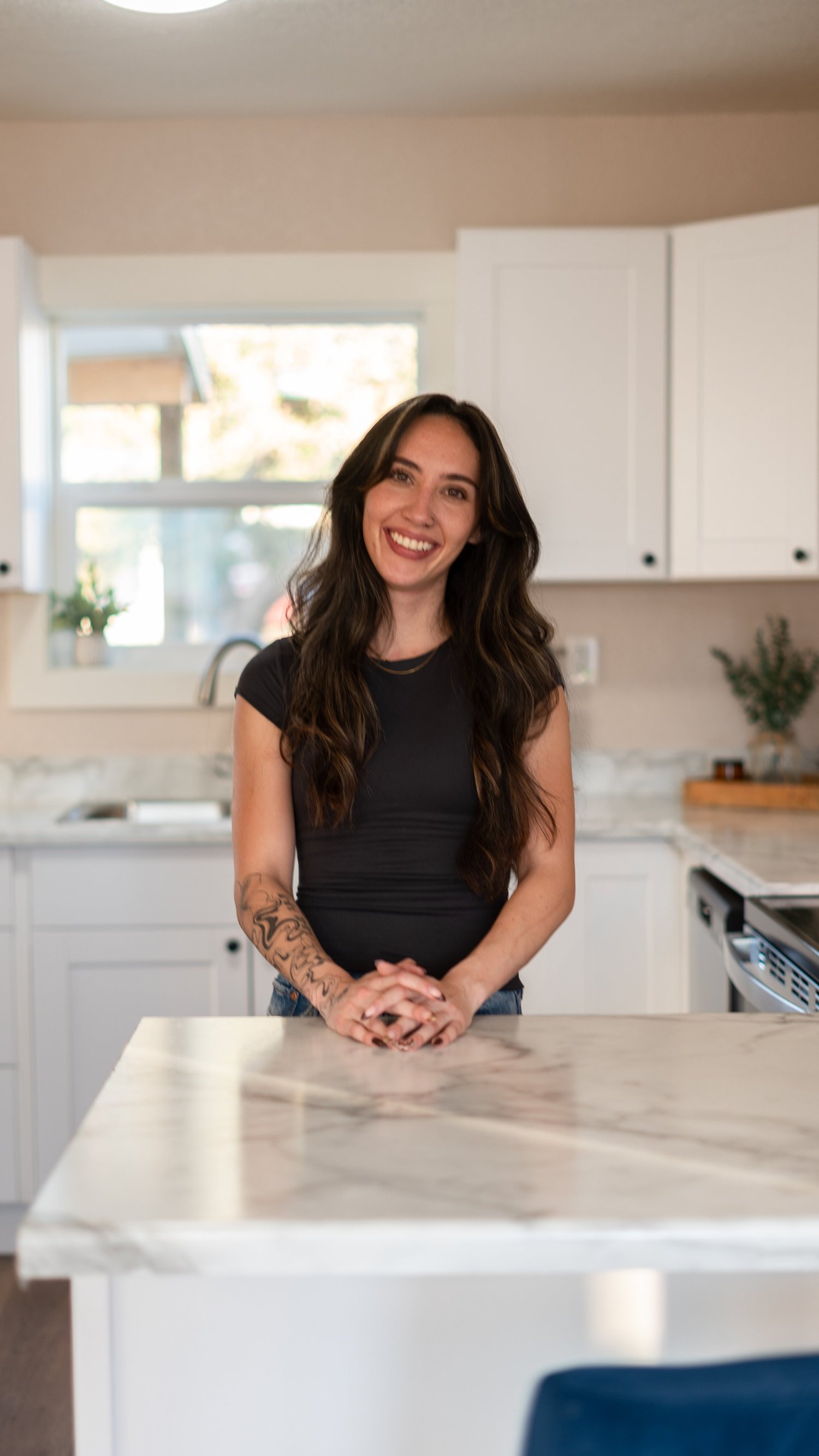 Portrait of a woman smiling with her head tilted beside a kitchen island.