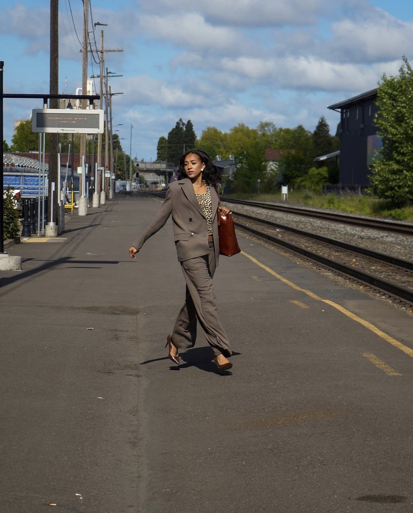 Full-length fashion portrait of a woman in a gray suit beside streetcar tracks.
