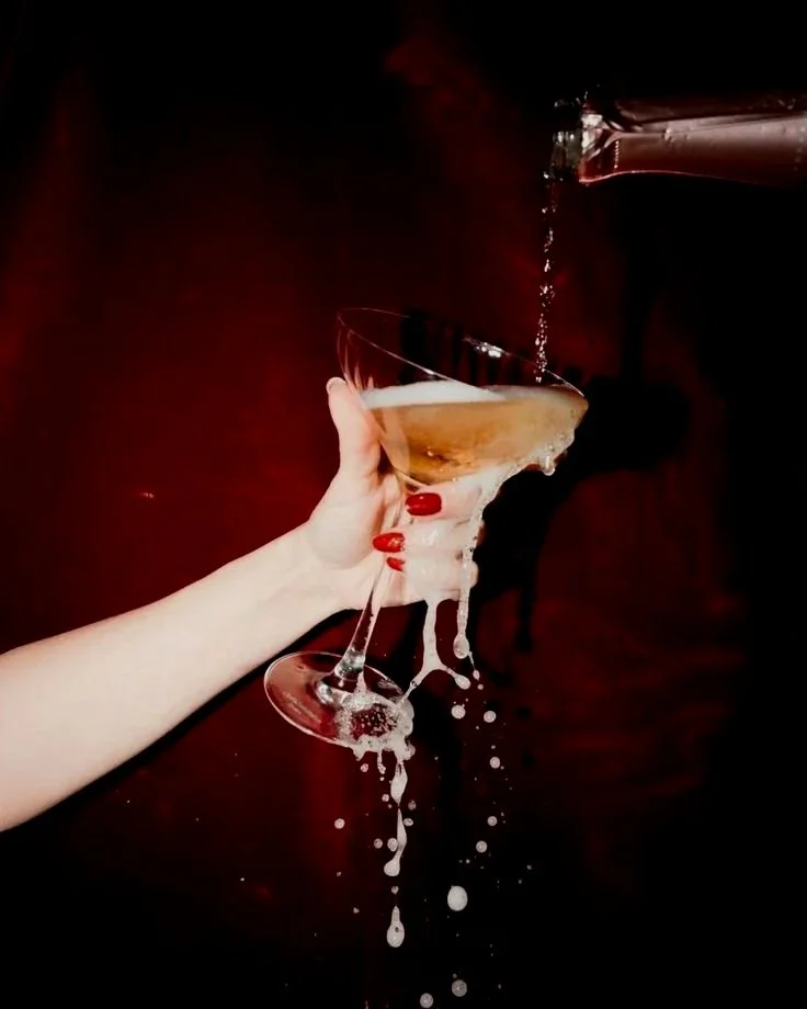 Champagne poured over a coupe against a red wall