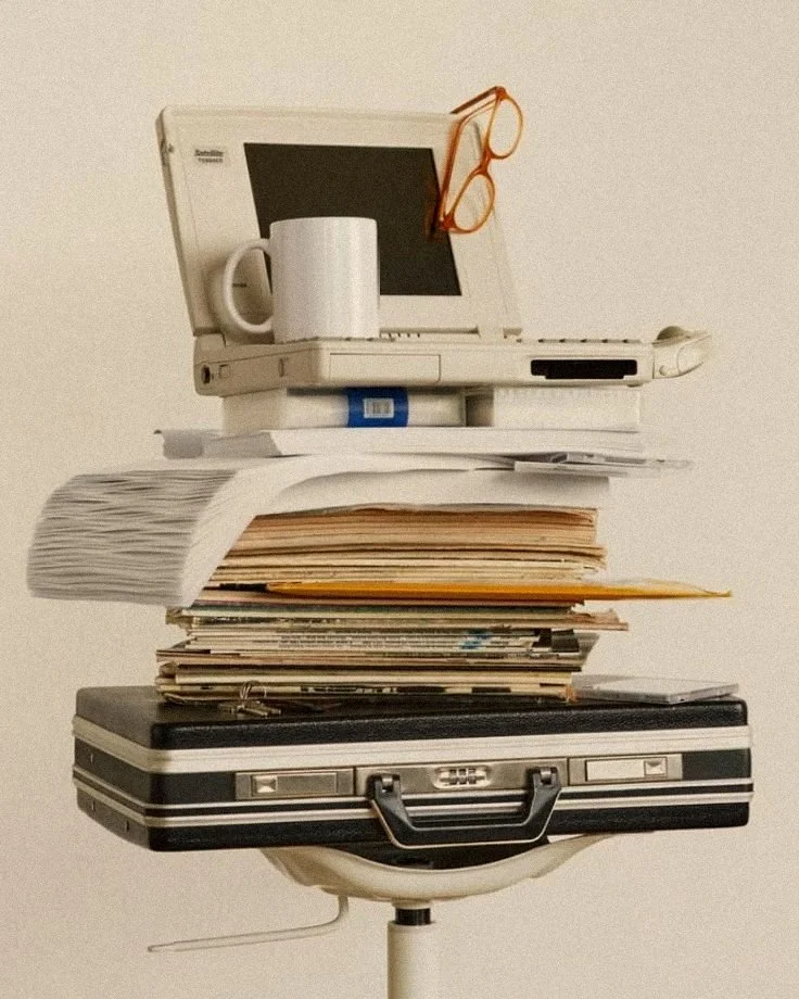 An owner’s Monday: a laptop, a mug, a stack of paperwork and a briefcase piled on an office chair