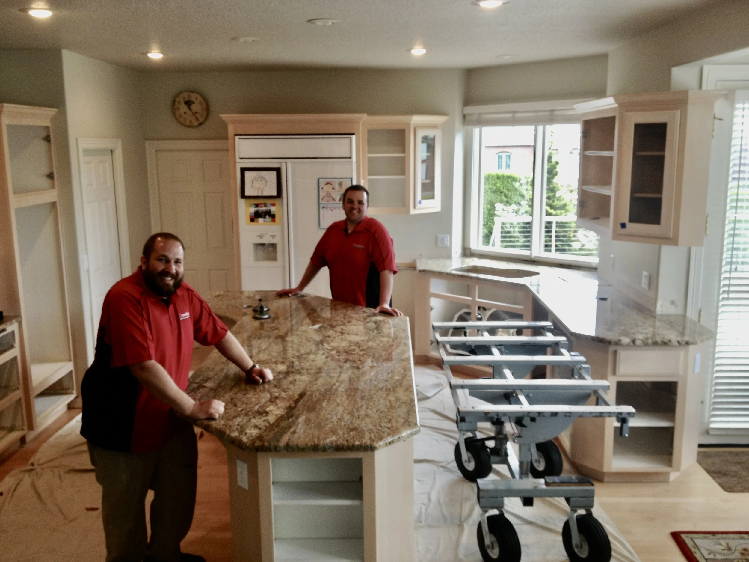 Two installers beside a large granite kitchen island, one of the first successful installations using the No Lift System slab installation cart