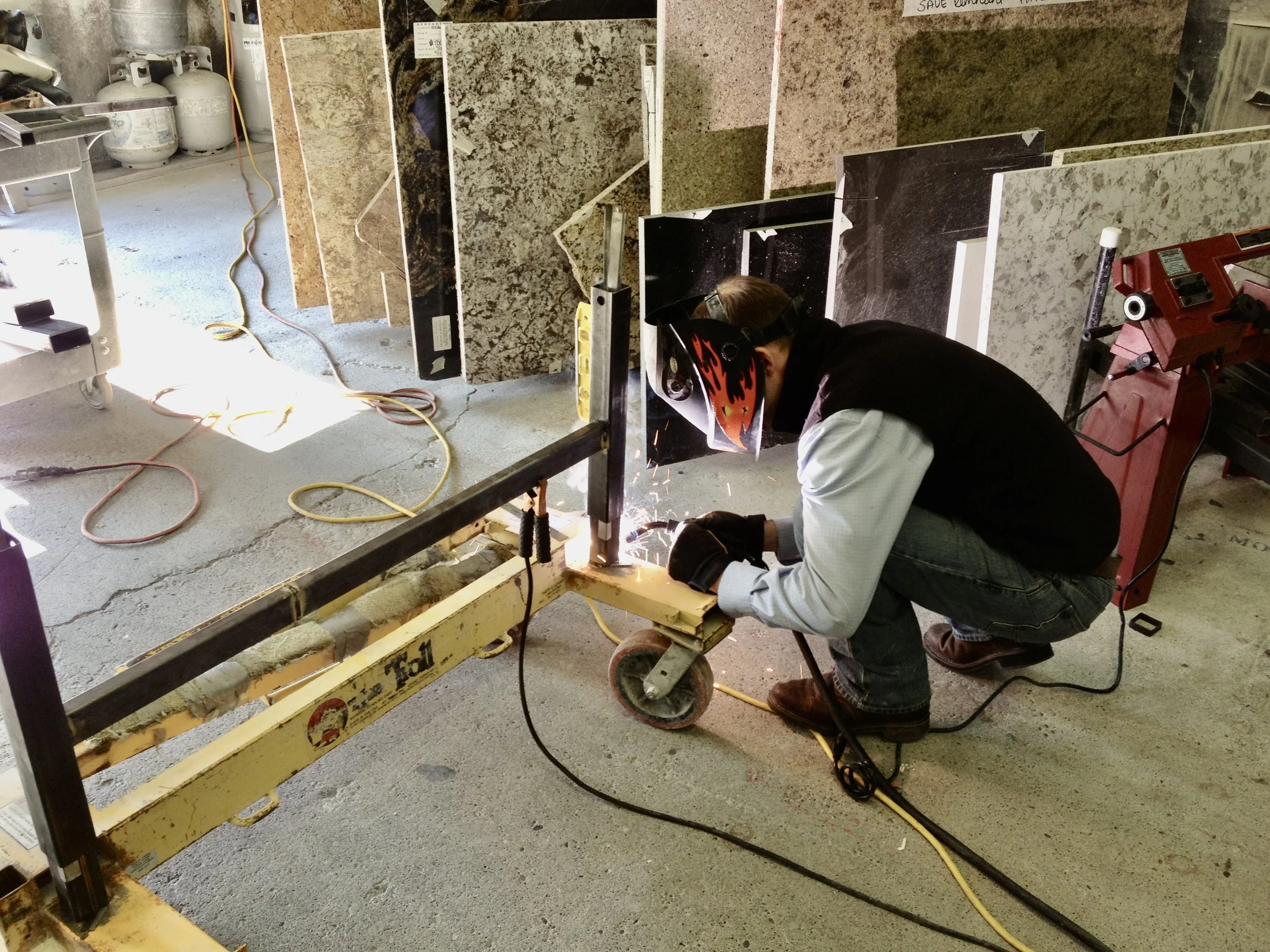 Welding the base of the first No Lift System install cart on a repurposed shop dolly in a stone fabrication shop