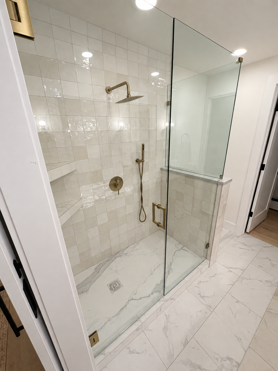 Glass enclosed shower with brass fixtures and marble look tile