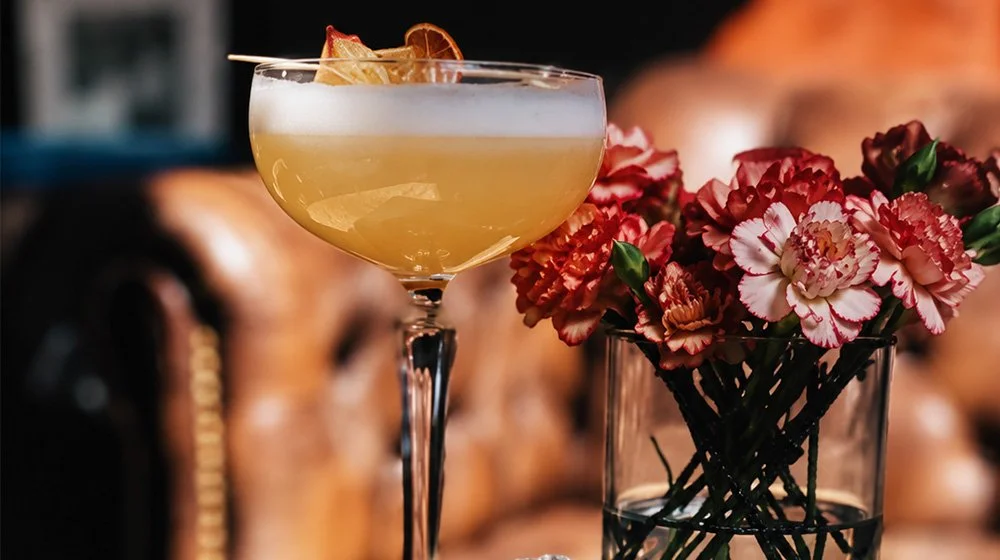 Elegant craft cocktail served in a coupe glass beside fresh flowers and vintage books at 205 Dry.