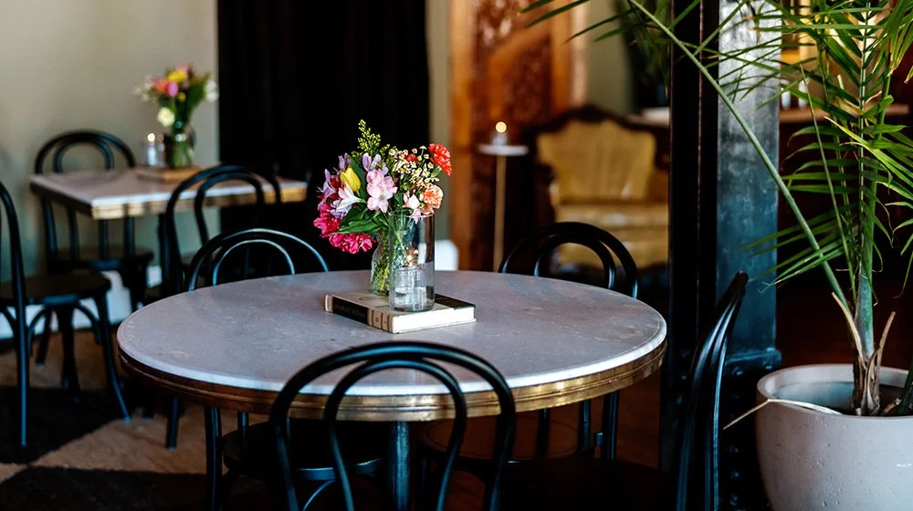 Table seating arrangement inside the Canopy Room at 205 Dry, featuring marble tables, floral centerpieces, and intimate event space décor.
