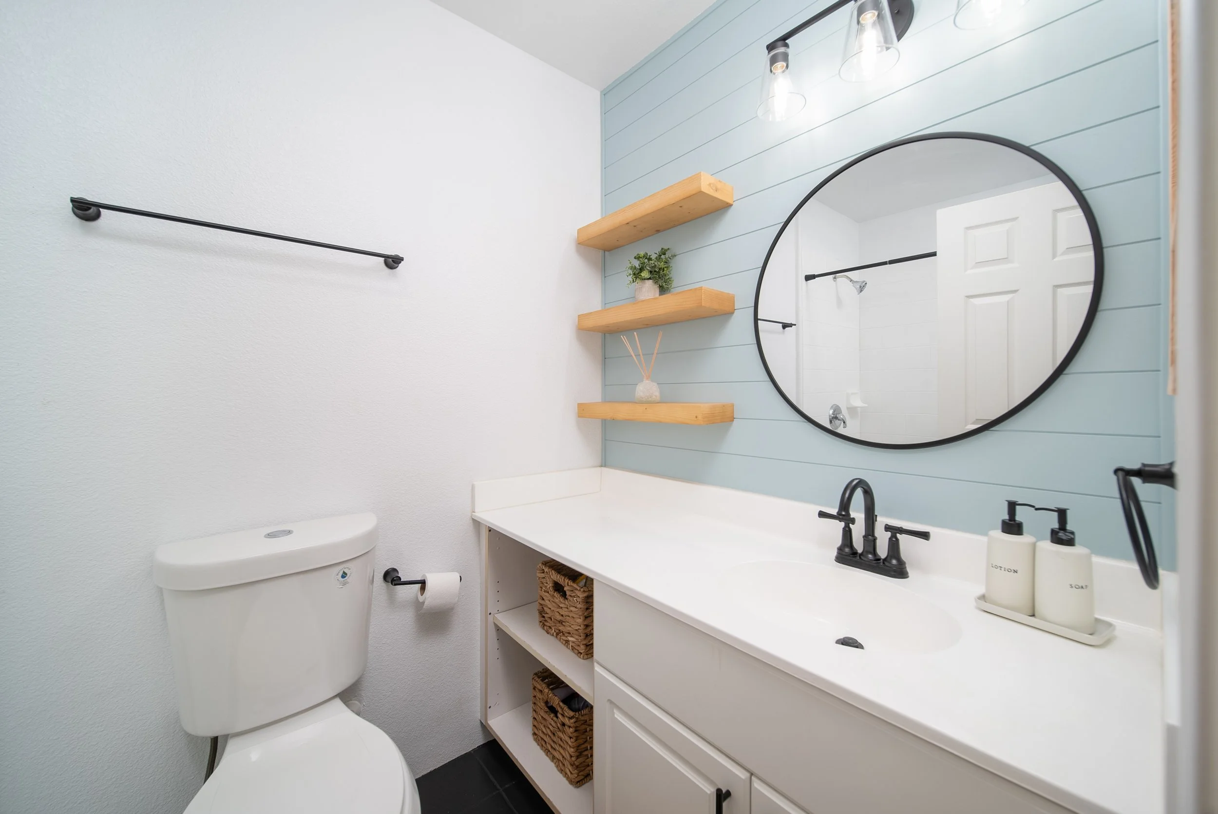Powder room with shiplap wall, round mirror and open wood shelving