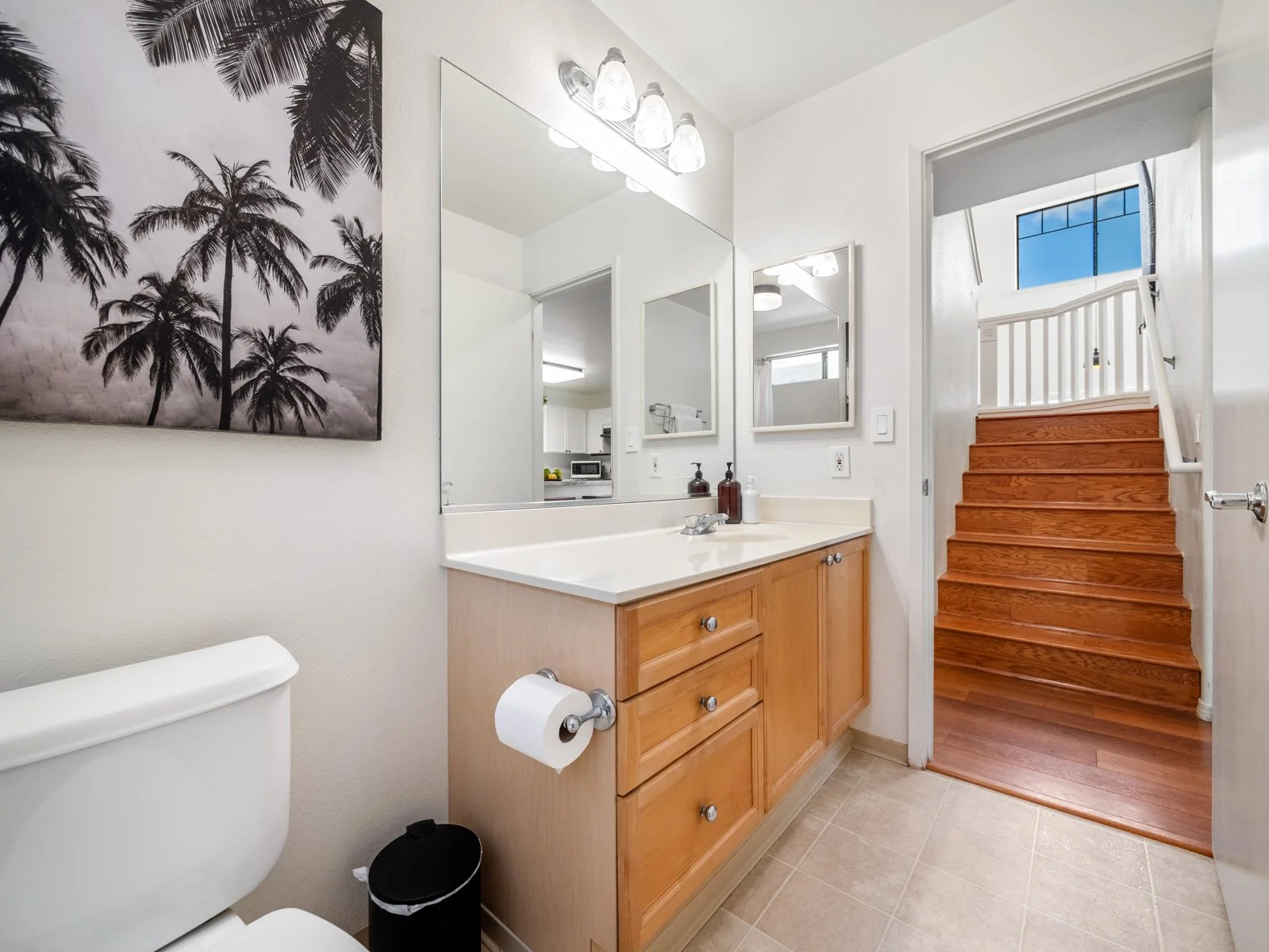 First floor bathroom with wood vanity, mirror and stairway beyond