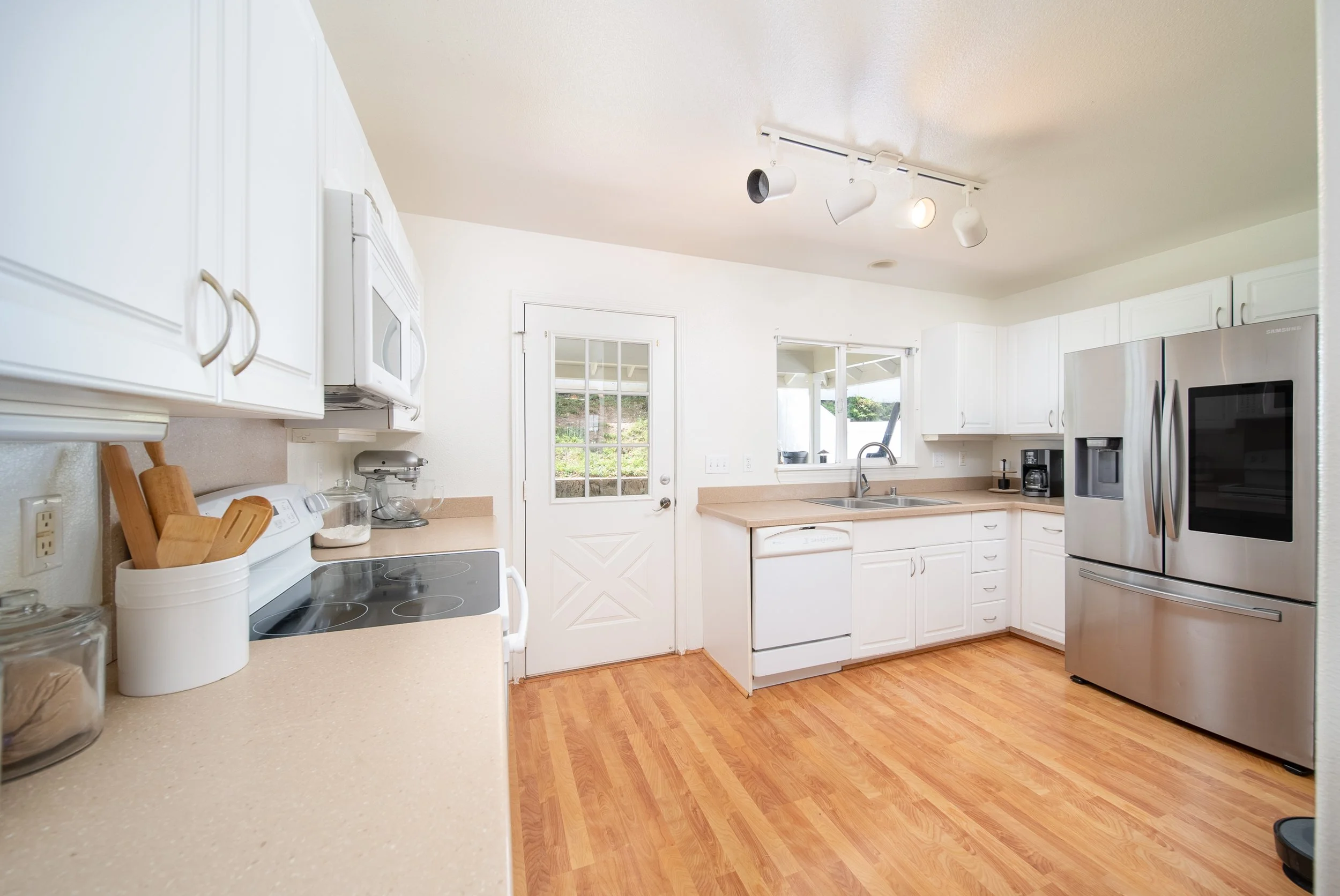 Kitchen with white cabinetry, stainless refrigerator and door to the yard