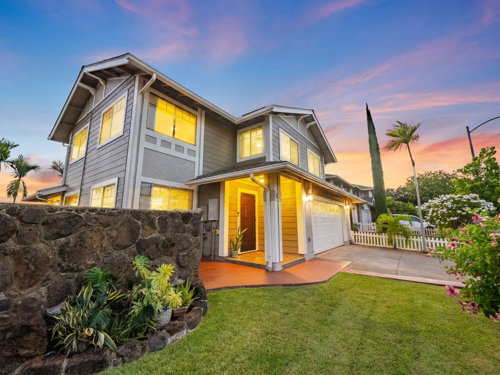 Twilight exterior with front lawn, rock retaining wall and lit entry