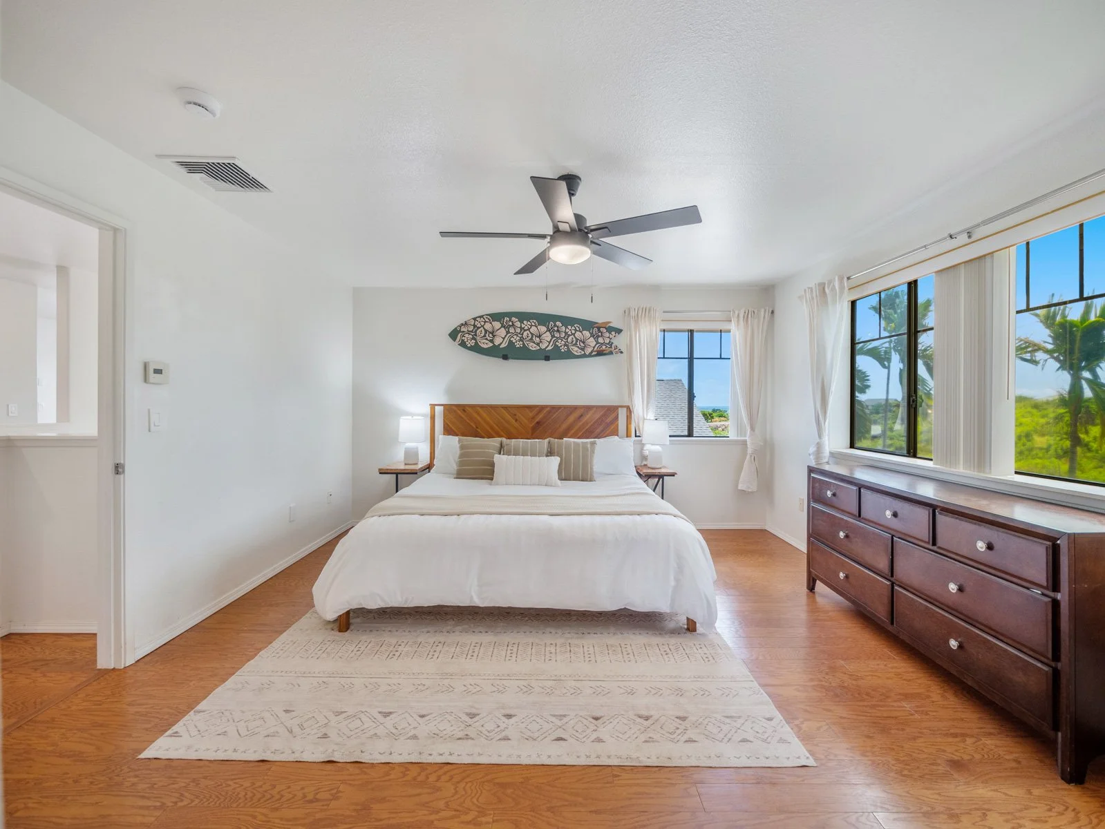 Primary bedroom with ceiling fan, wood dresser and windows to the green space