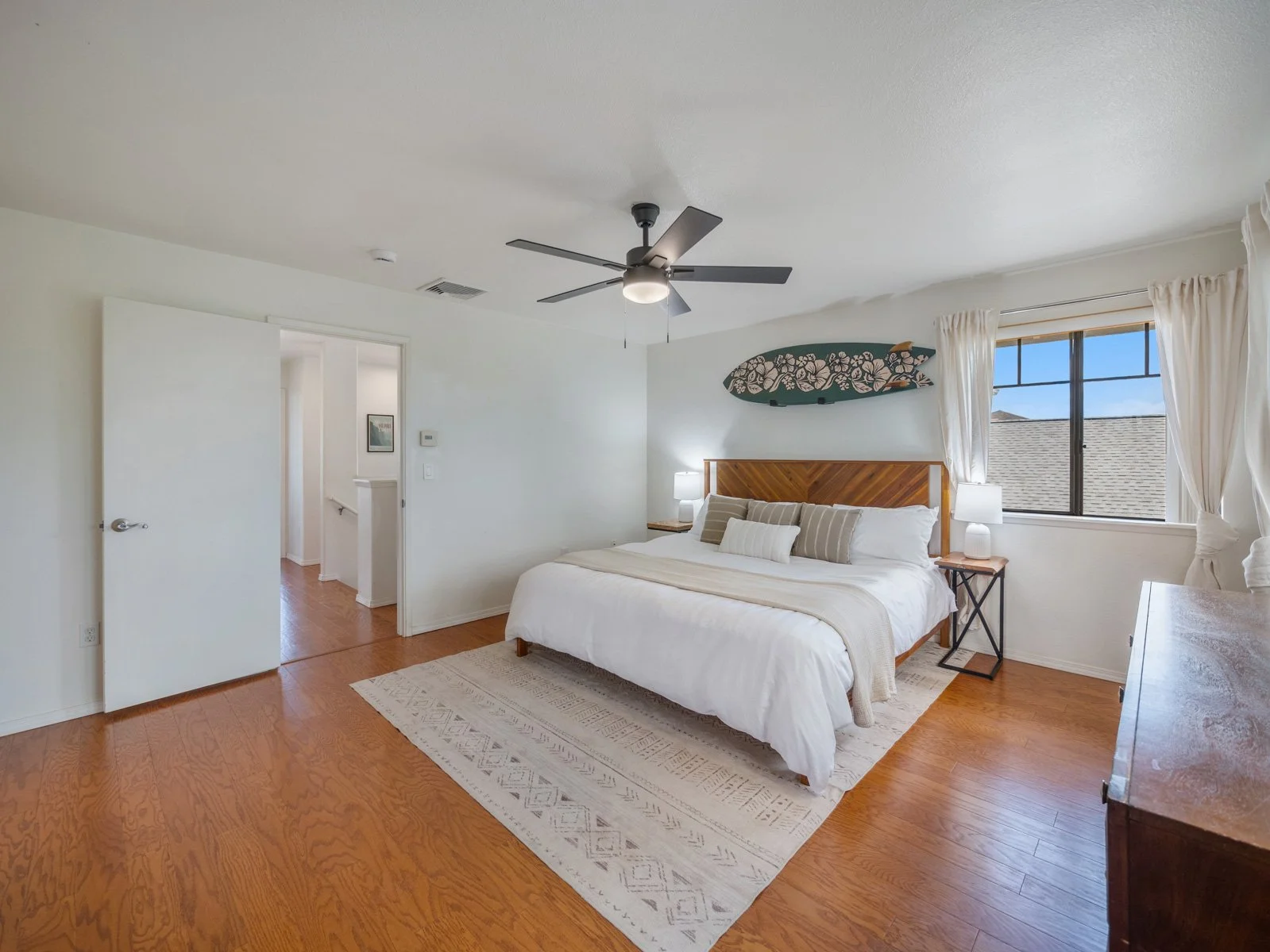 Primary bedroom with hardwood floors, ceiling fan and doorway to the bathroom