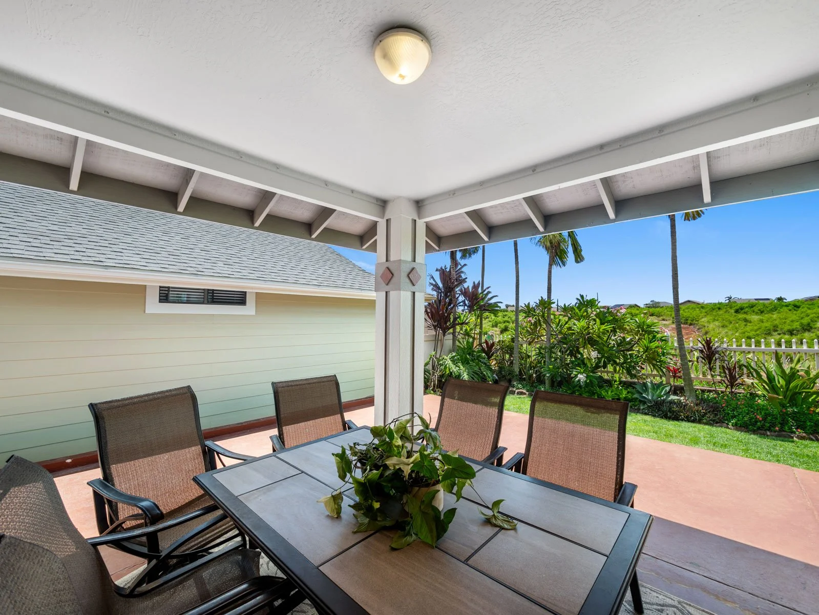 Covered lanai with dining set looking out to the fenced lawn and greenery