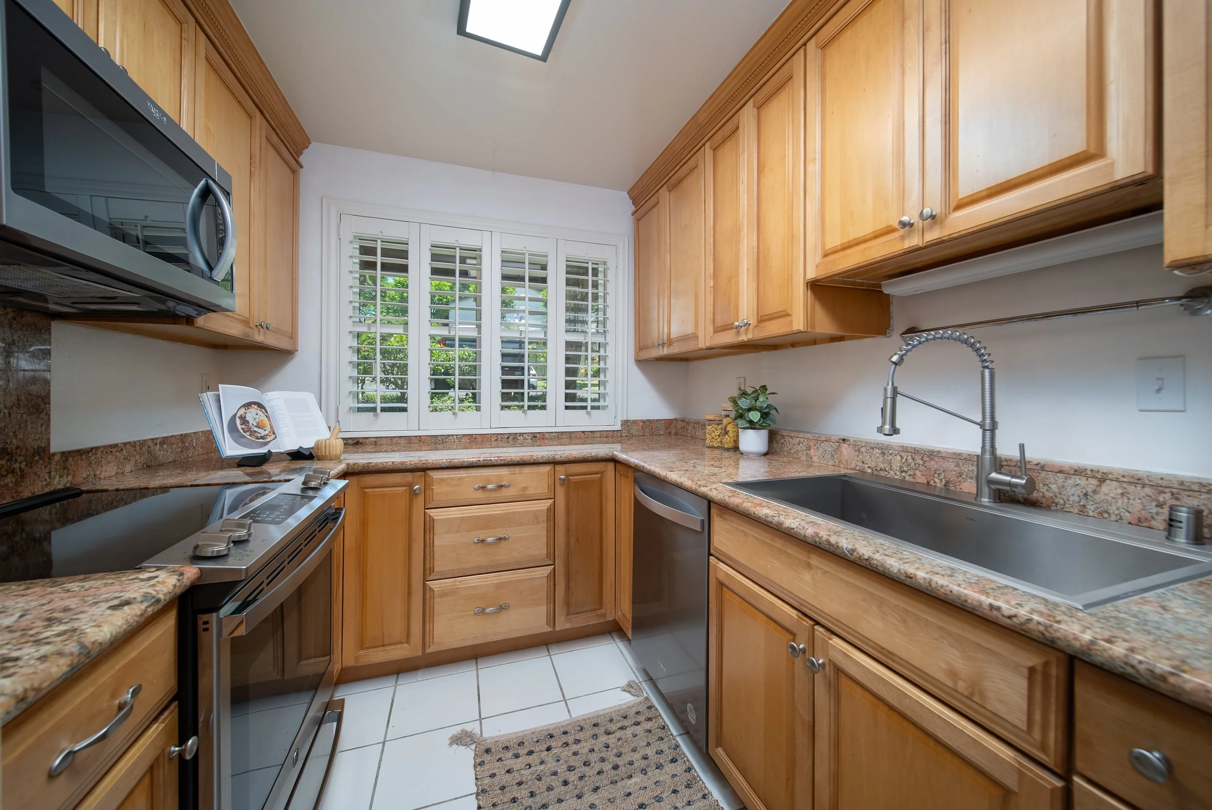 Kitchen with wood cabinetry, granite counters, range and window above the sink