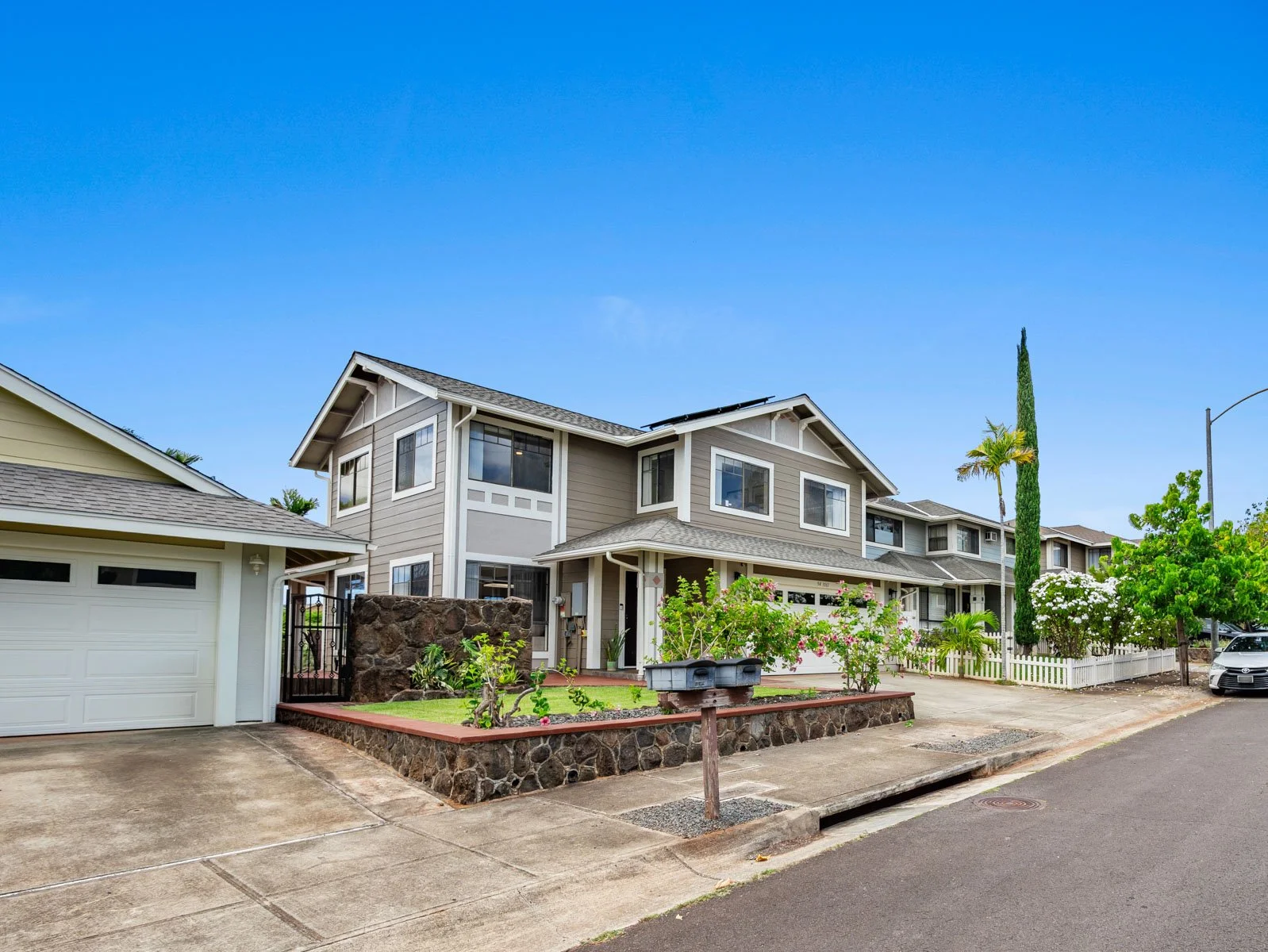Street view of the two story exterior with garage and rock wall