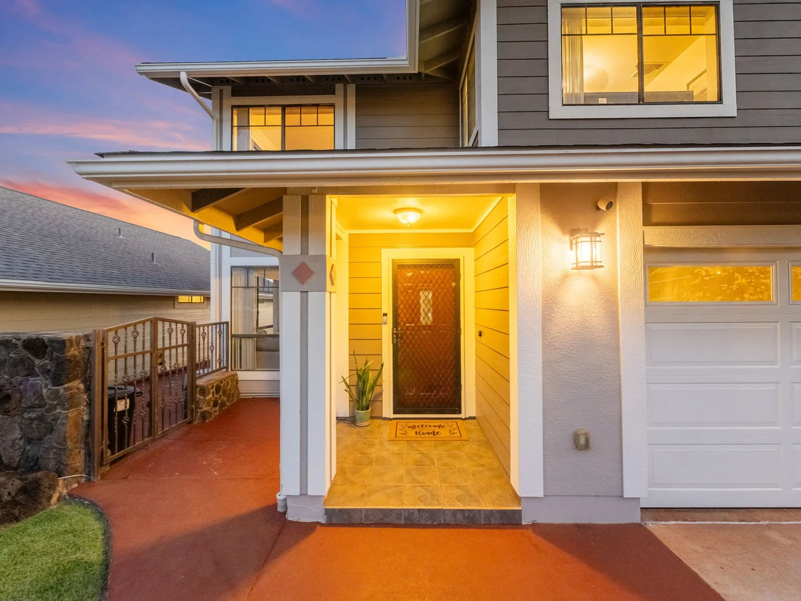 Lit front entry with wood door, covered porch and gated side walkway