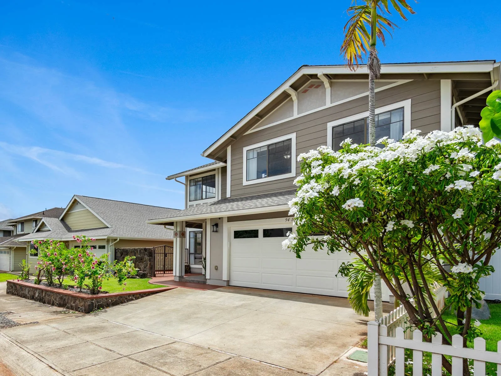 Daytime front elevation with driveway, plumeria tree and picket fence