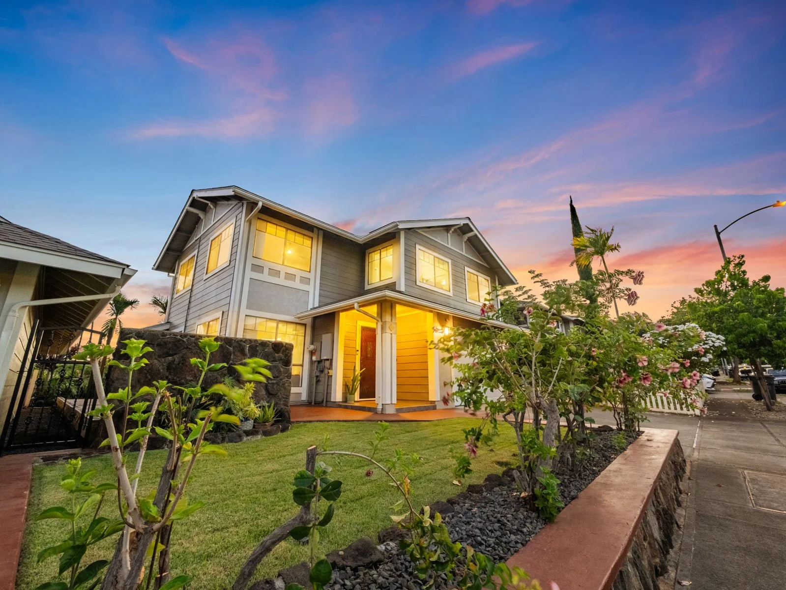 Twilight front elevation with lit windows, lawn and flowering plants