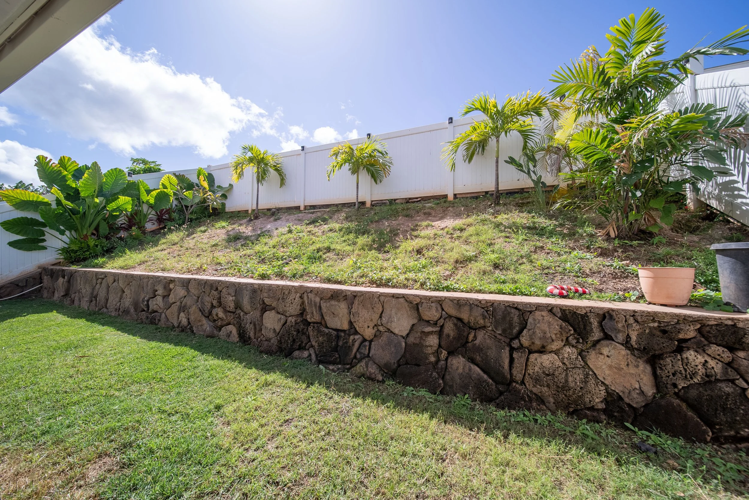 Fenced backyard with rock retaining wall, palms and tropical planting